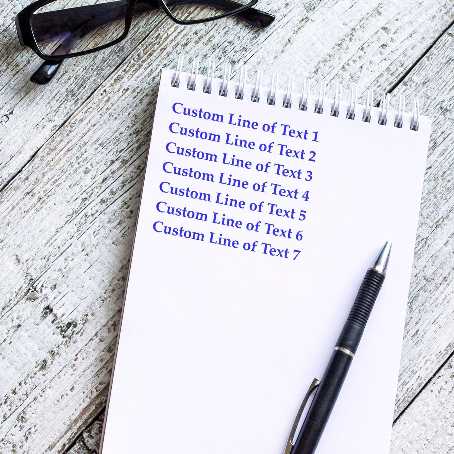 Customizable notebook page with blue placeholder lines for custom text, with pen and eyeglasses on rustic wooden desk template.