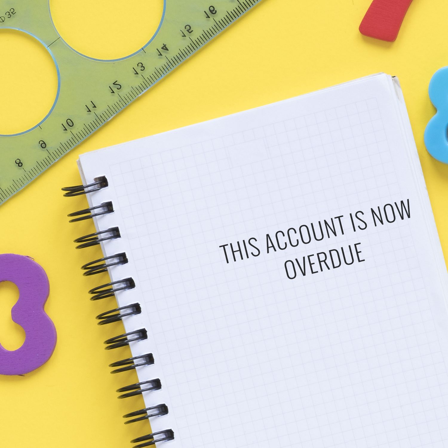Overdue payment reminder: notebook page says This account is now overdue beside a ruler and colorful shapes.