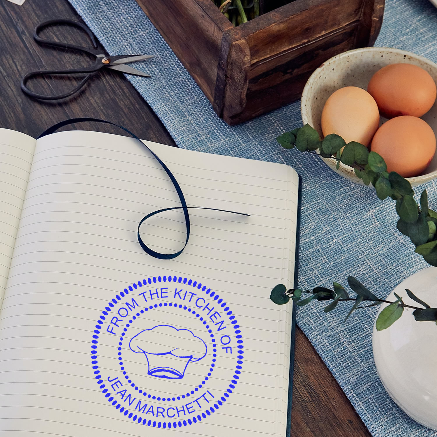 Custom kitchen rubber stamp reading From the Kitchen of Jean Marchetti with chef hat logo on an open notebook.