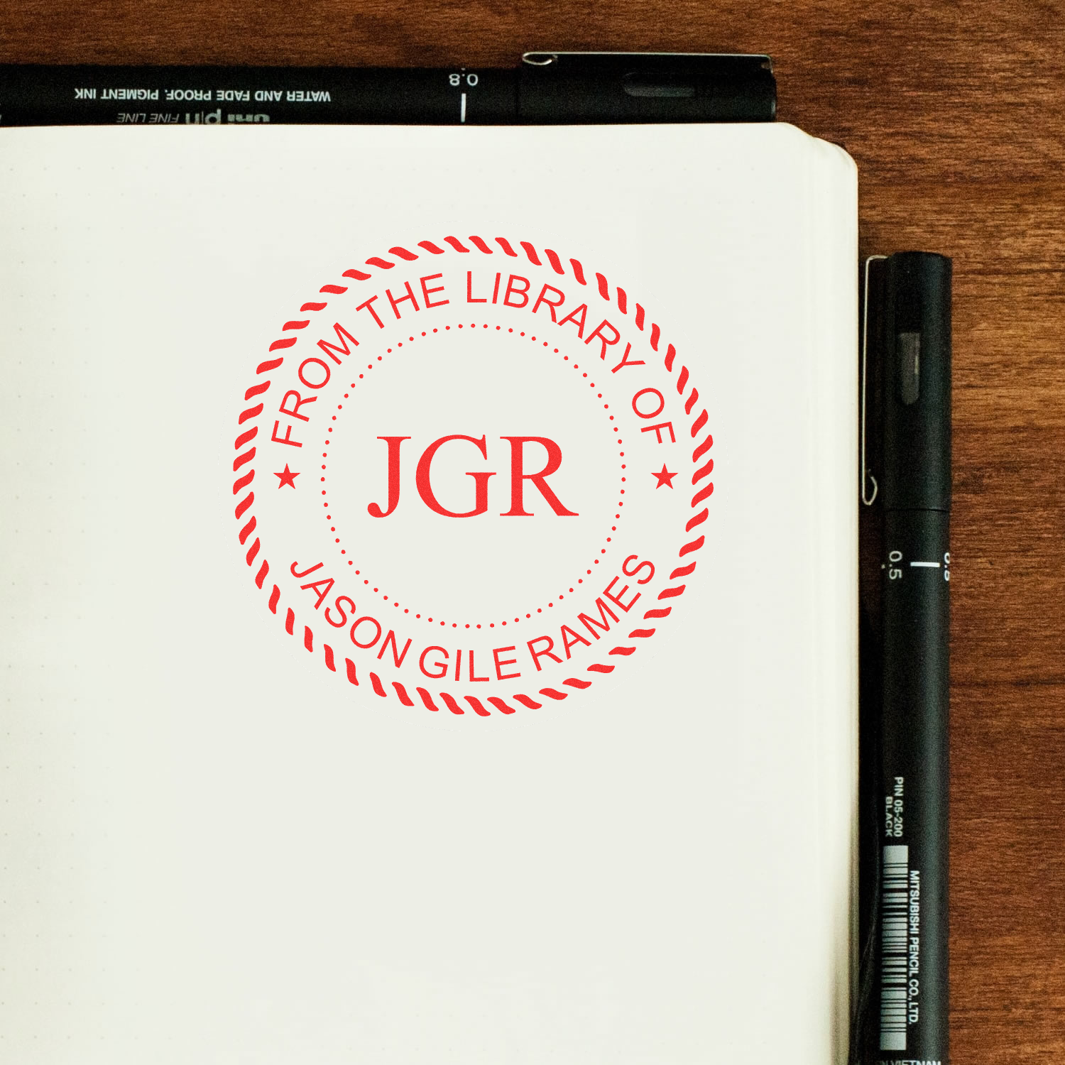 Notebook page with From the Library of JGR stamp and pen on wooden desk, showing library book ownership labeling.