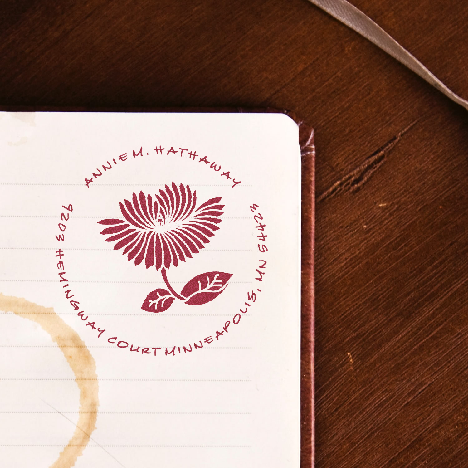 Custom return address rubber stamp with floral logo on a notebook page, ideal for personalized stationery and mailing.