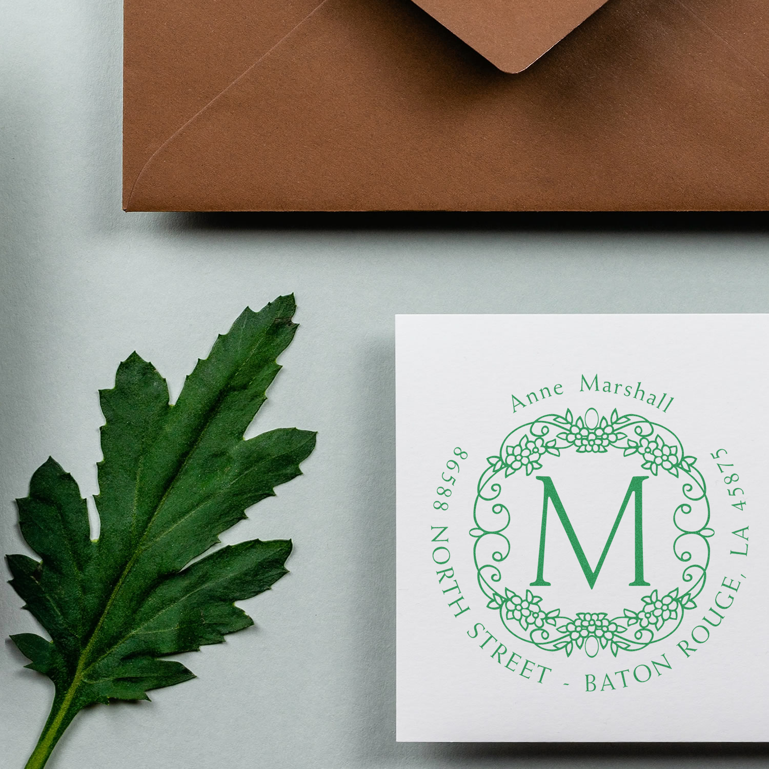 Custom rubber stamp with floral monogram return address in green ink on stationery, envelope, and leaf.