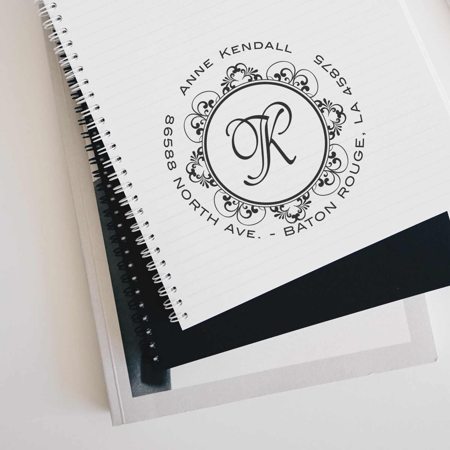Personalized monogram return address rubber stamp with floral border, shown on a notebook page