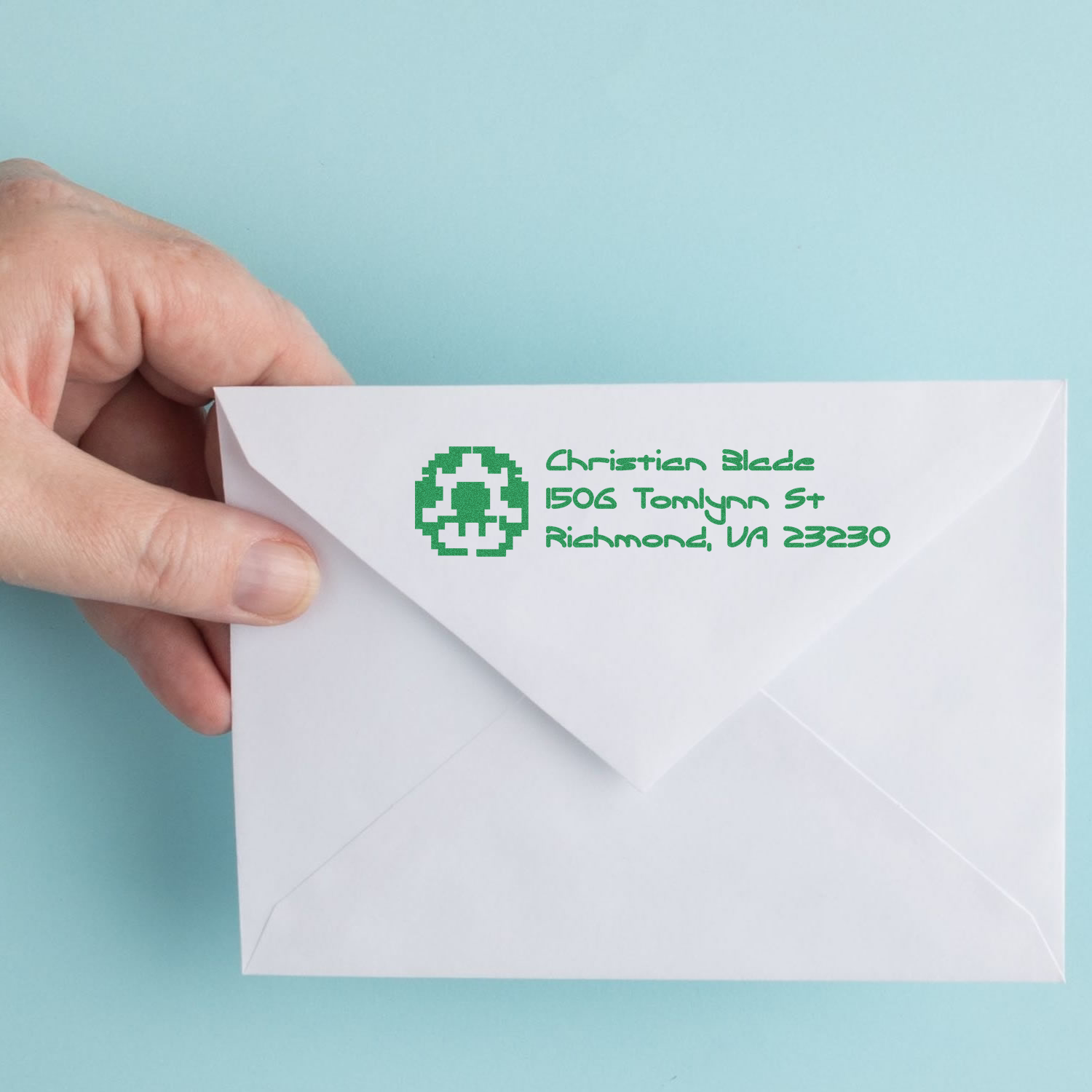 Hand holding envelope with custom return address rubber stamp in green ink for mailing letters.