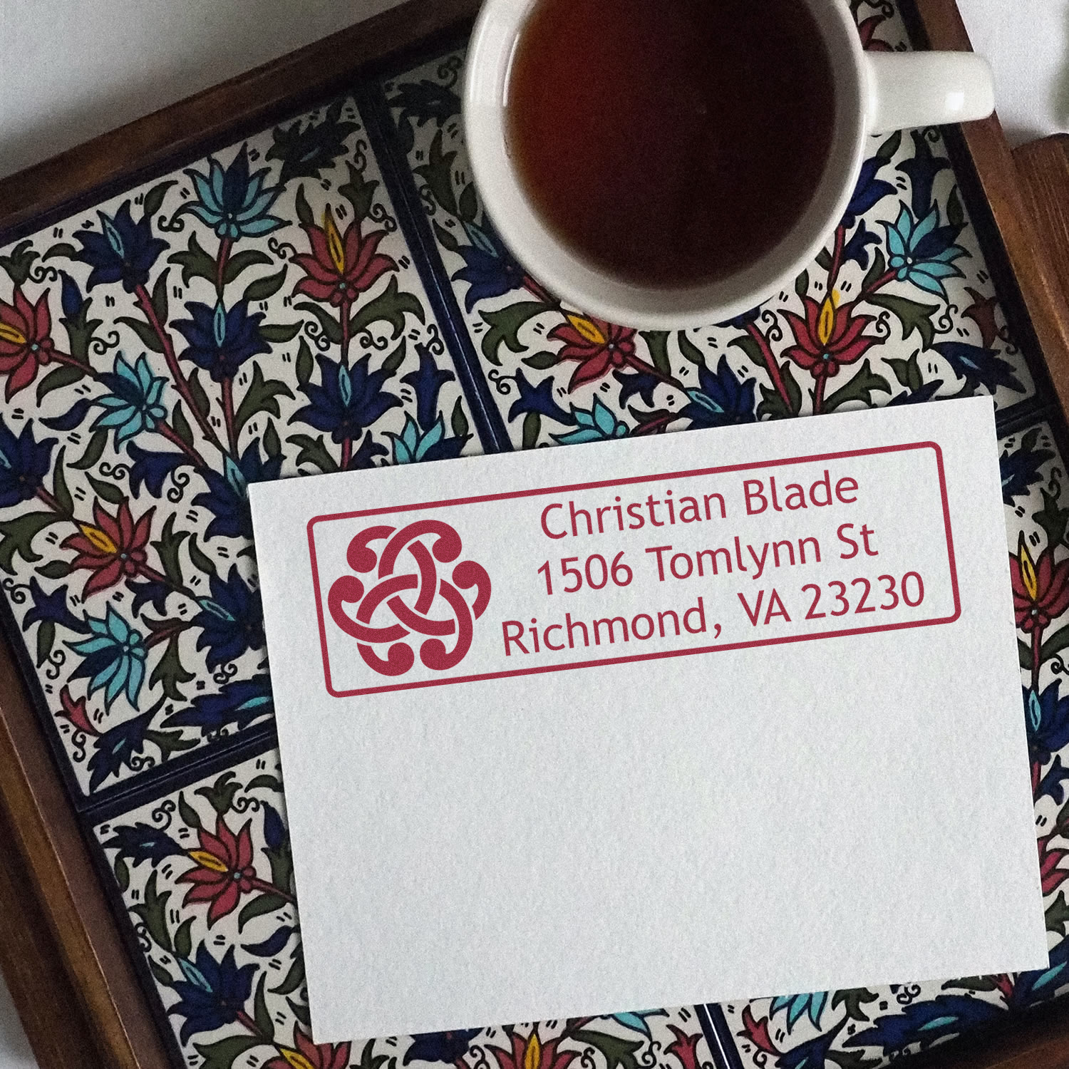 Custom return address rubber stamp on envelope with name and Richmond, VA address, beside a cup of tea.