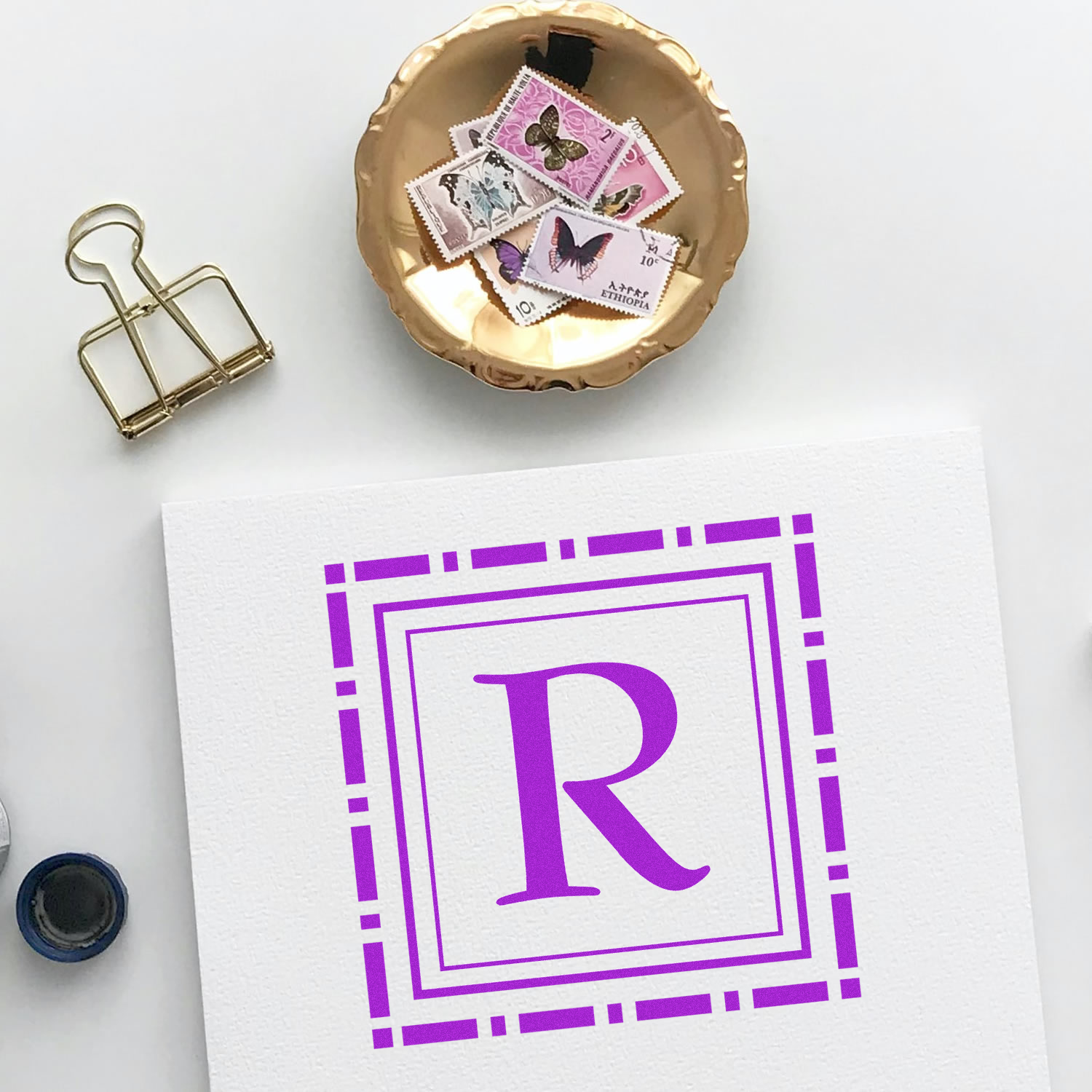 Purple monogram R rubber stamp impression on white paper with desk accessories, ideal for custom stationery branding.