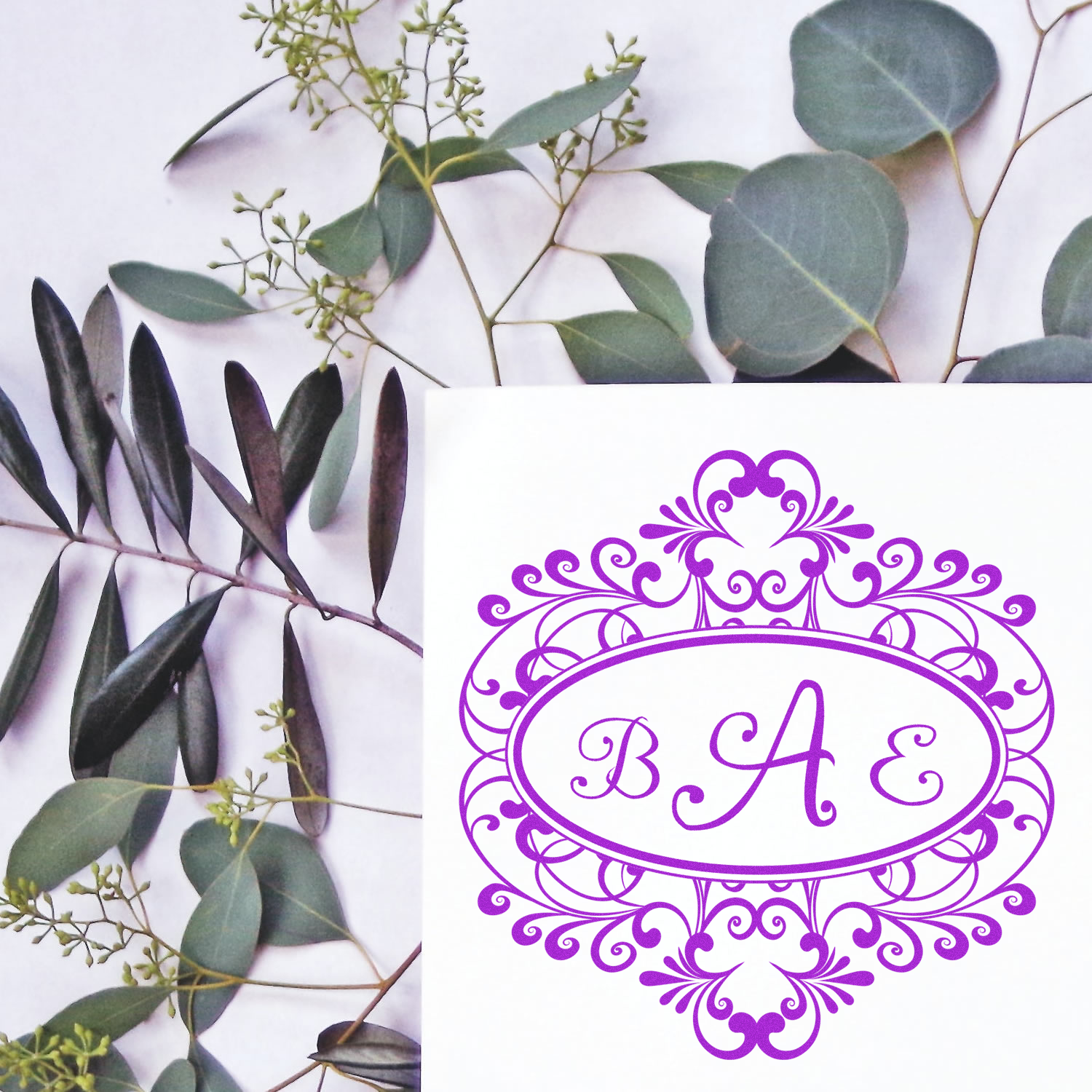 Ornate BAE monogram rubber stamp design in purple on white card with eucalyptus leaves, ideal for elegant custom branding.