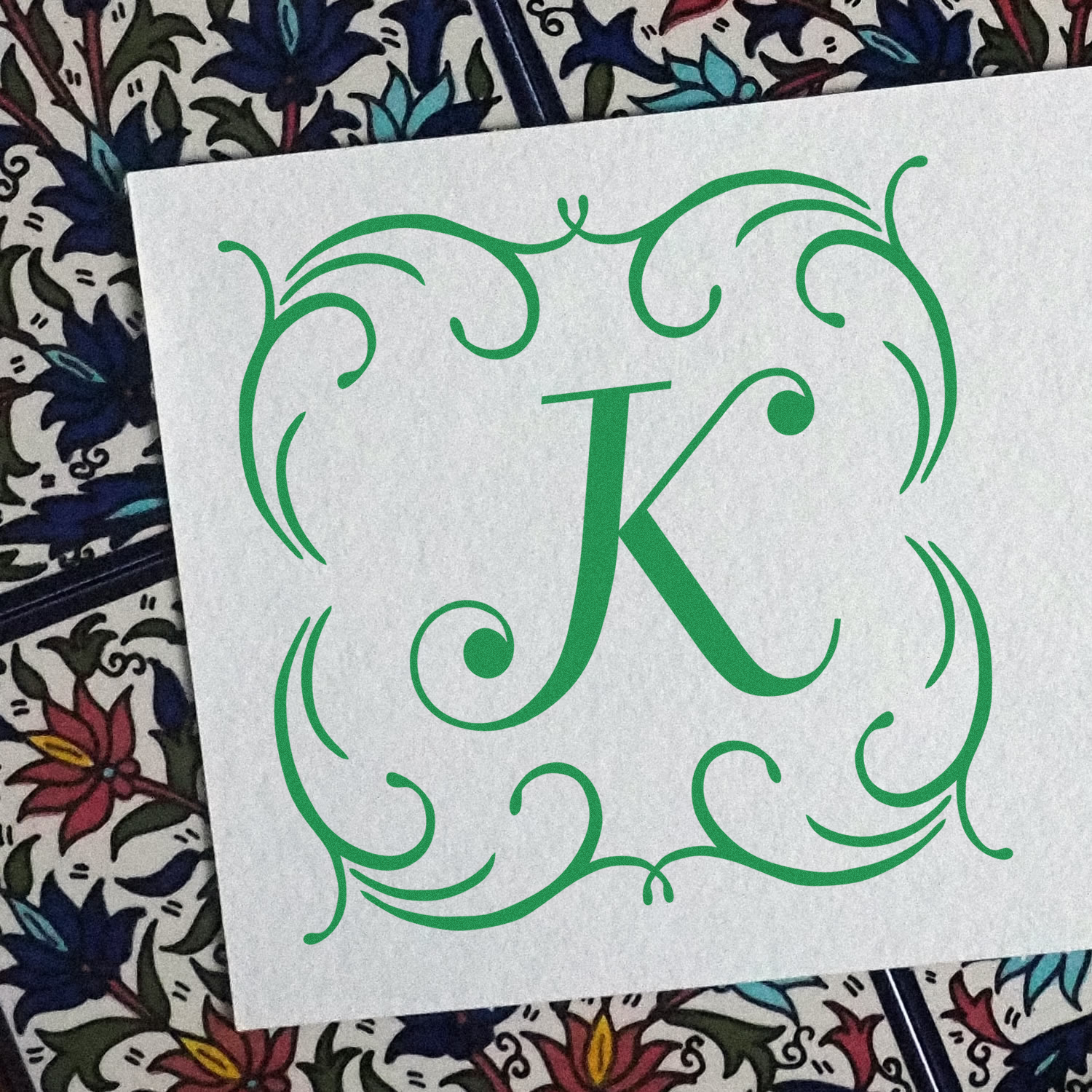 Custom rubber stamp design featuring a green ornate monogram K with decorative scroll frame.