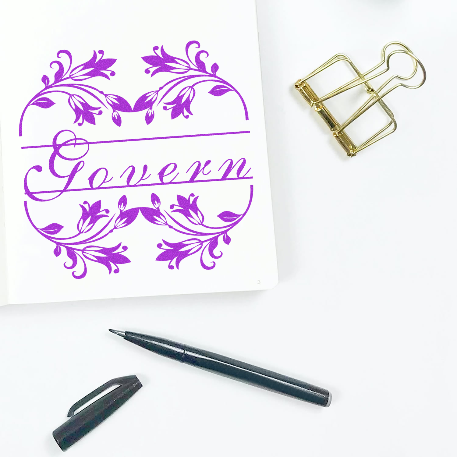 Custom floral rubber stamp with elegant monogram name for personalized stationery, shown with pen and paperclip.