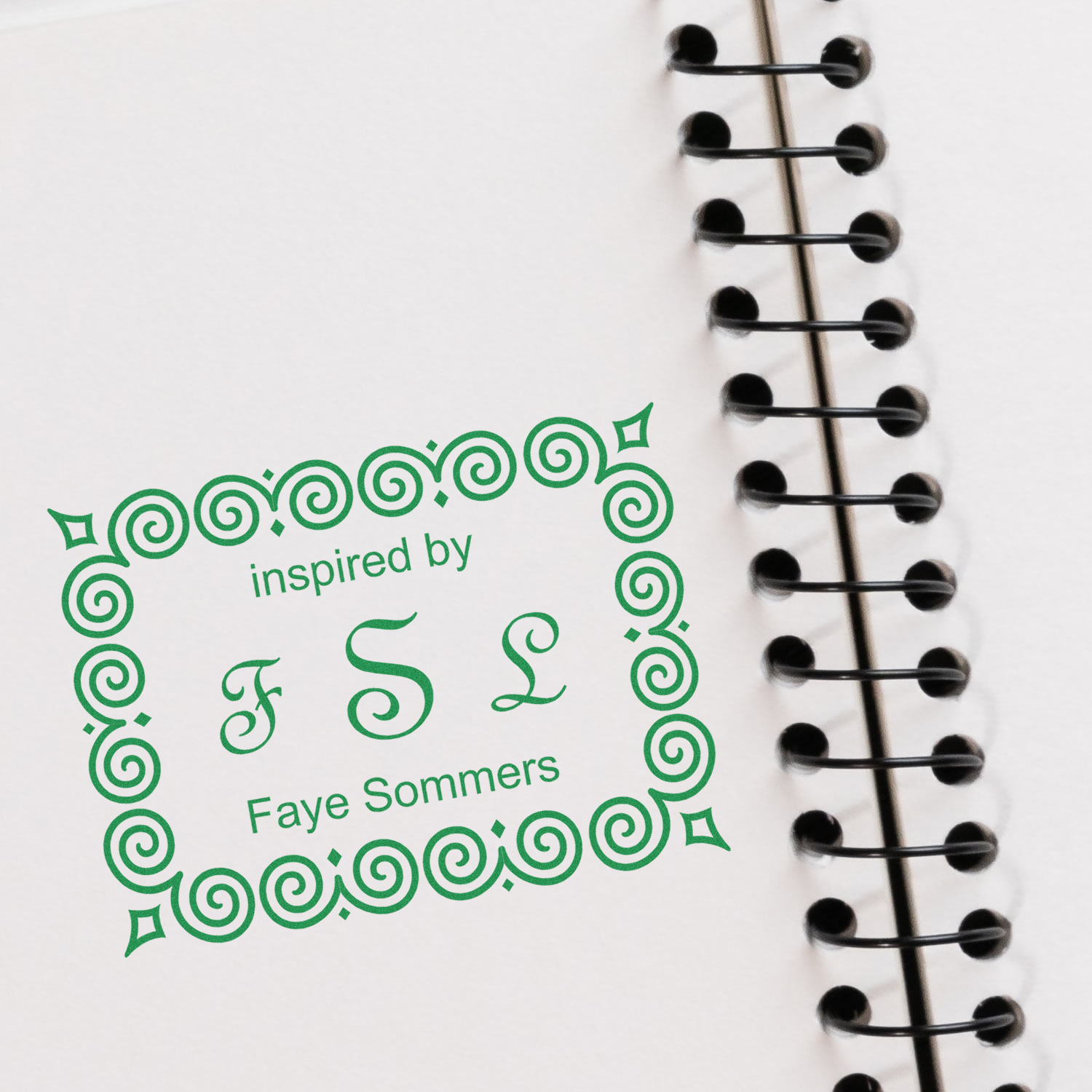 White spiral notebook with black rings featuring green Inspired by Faye Sommers logo for stationery branding.