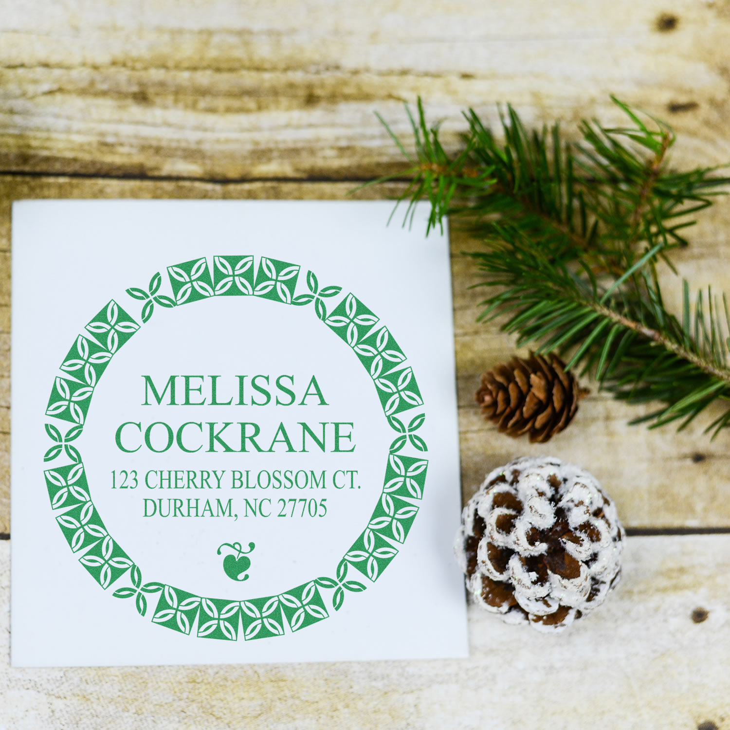 Custom rubber return address stamp with leaf border for Melissa Cockrane, shown on a holiday card with pinecone.