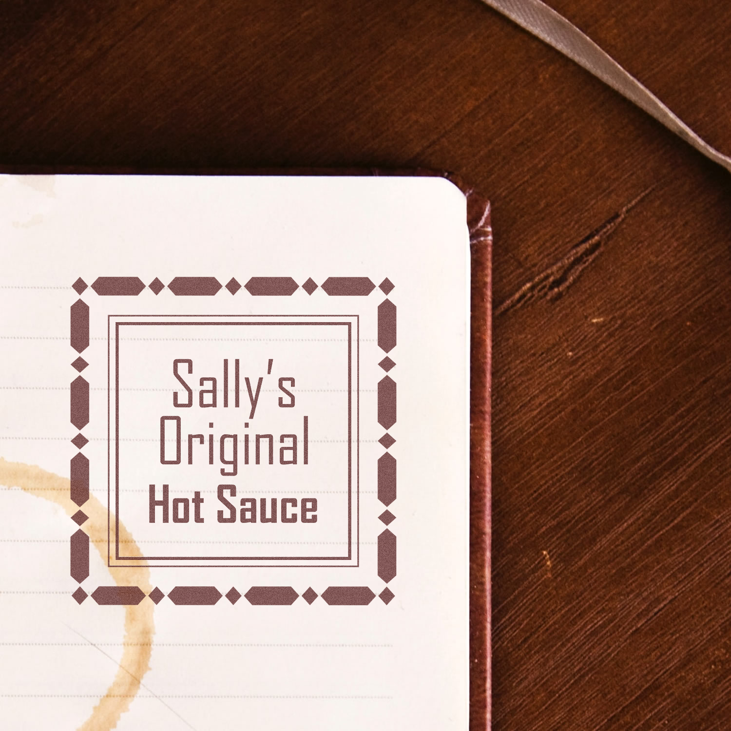 Custom rubber stamp mockup for Sallys Original Hot Sauce logo with vintage border on notebook paper.