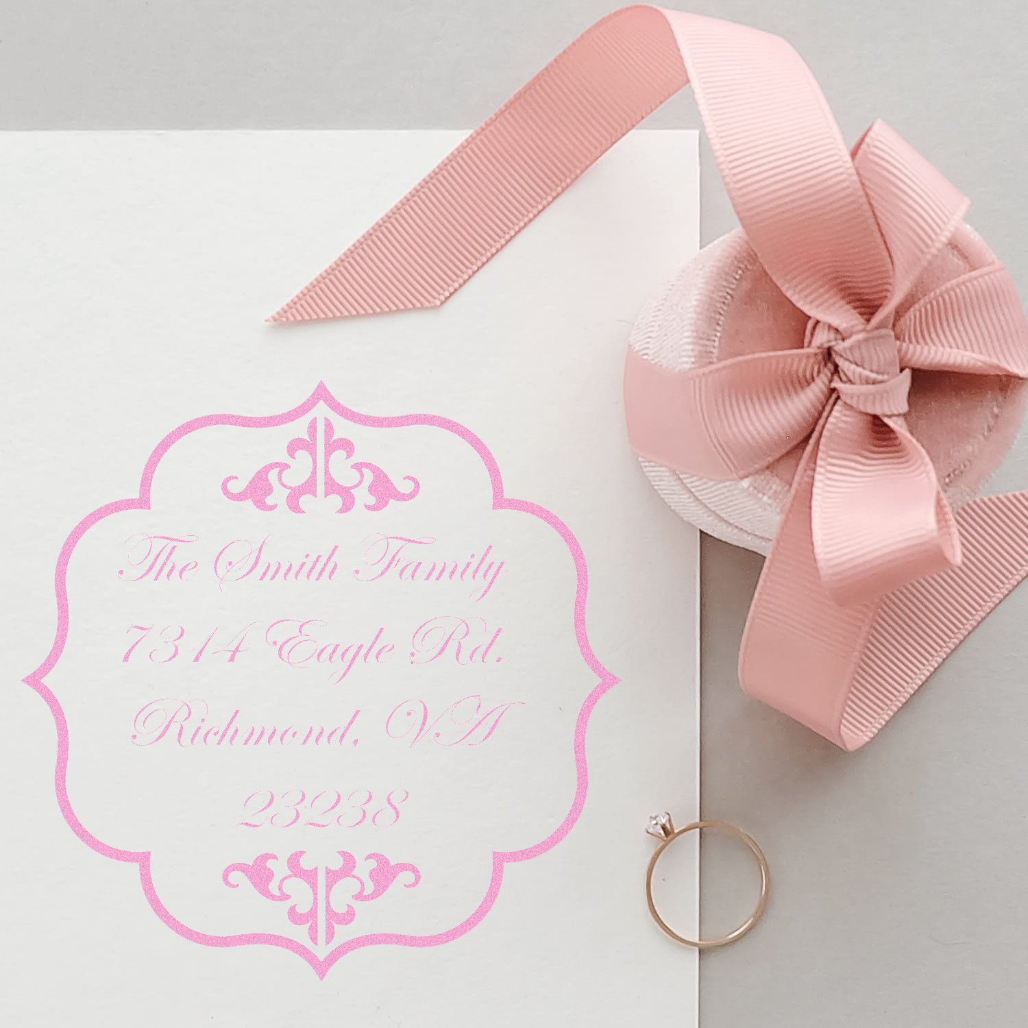 Custom pink rubber address stamp on wedding invitation envelope with decorative monogram, ribbon, and return address for The Smith Family.