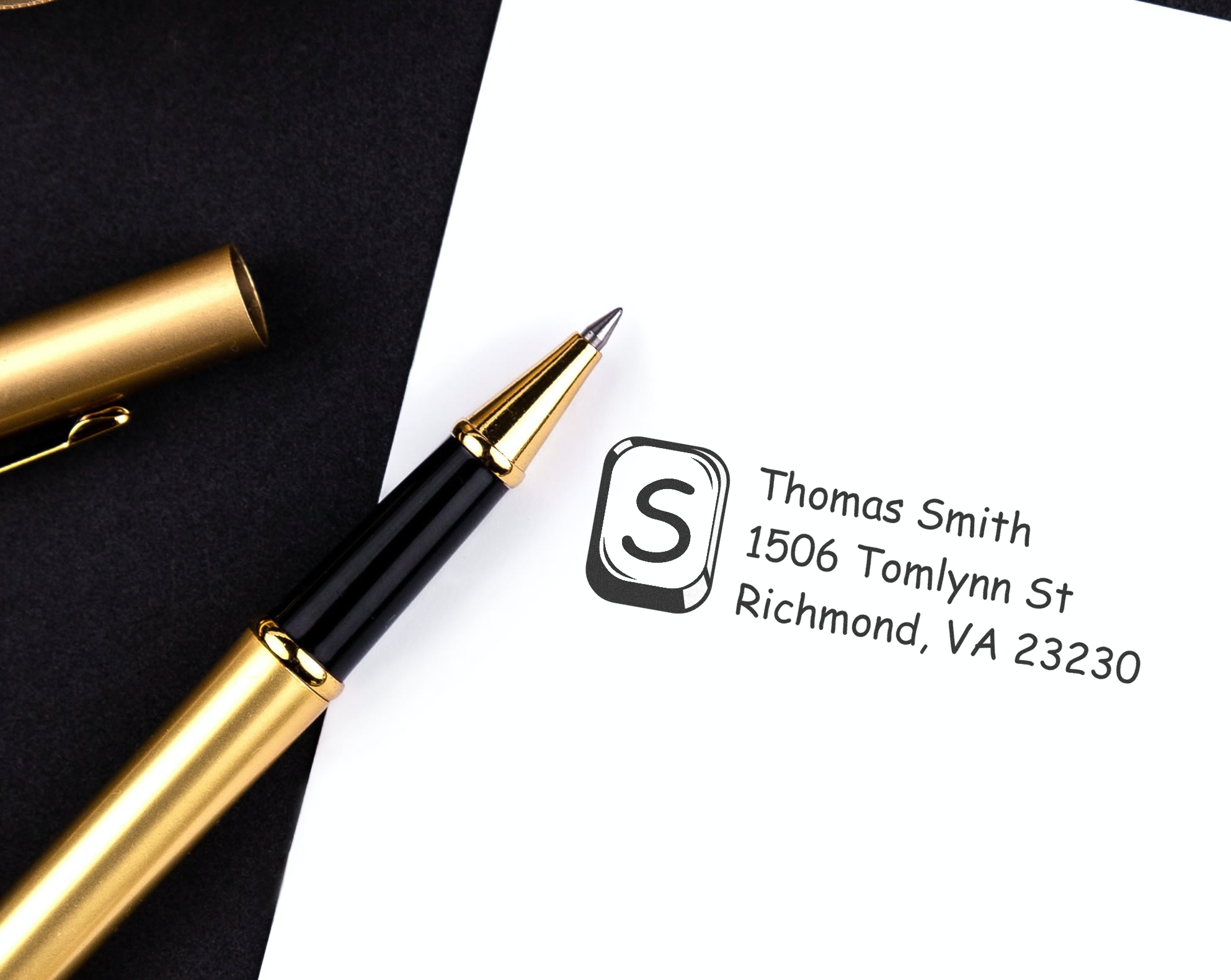 Custom rubber address stamp with name and mailing address beside gold pen for personal or business correspondence.