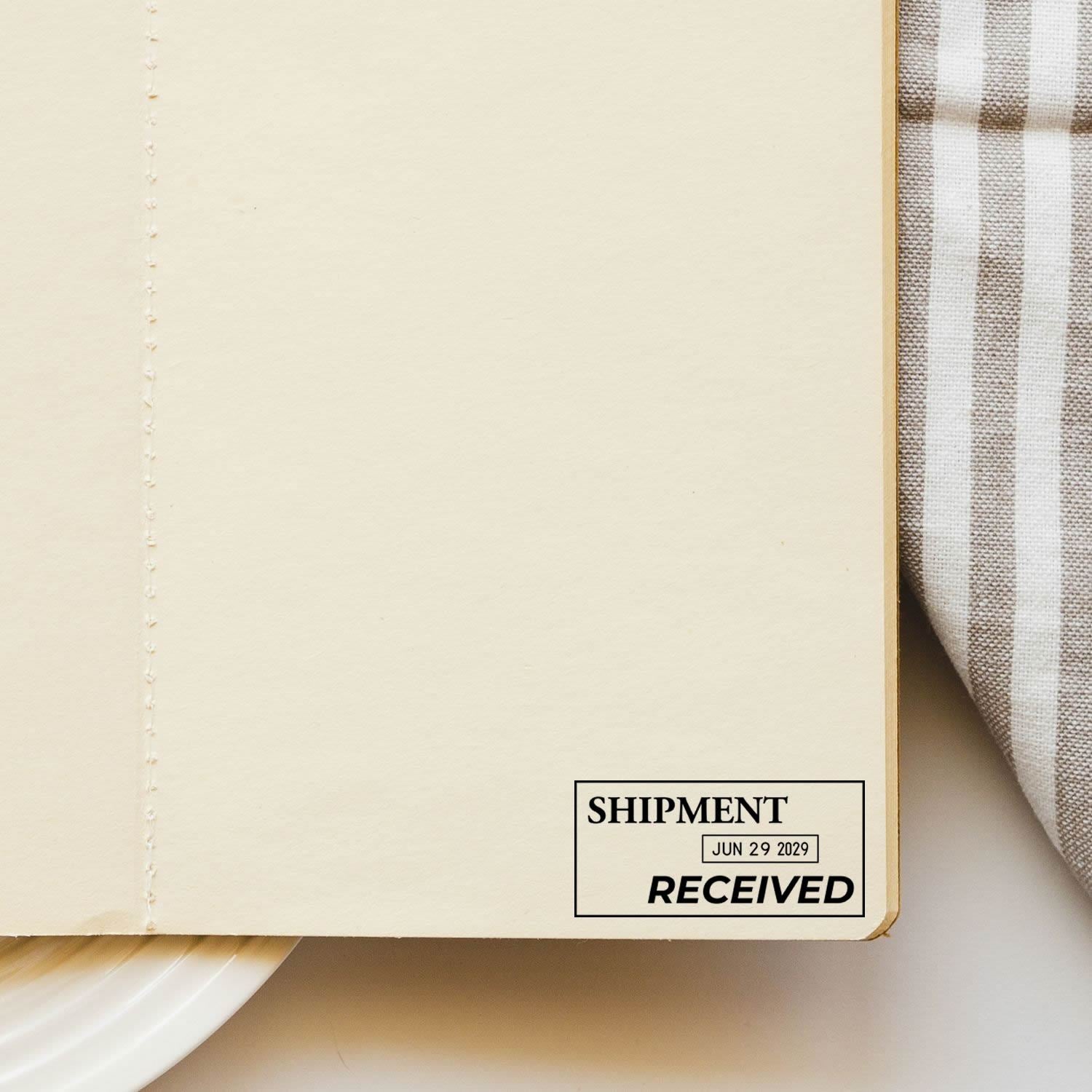 Close-up of a blank cream notebook page with Shipment Received stamp and striped fabric background.