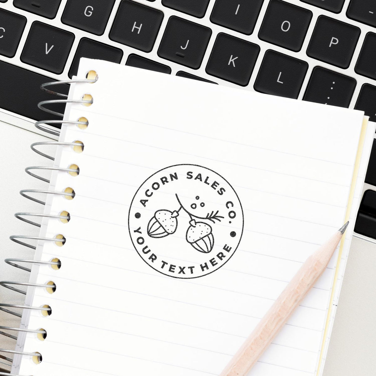 Notebook with Acorn Sales logo on lined pages beside pencil and keyboardcreative office branding for marketing ideas and strategy
