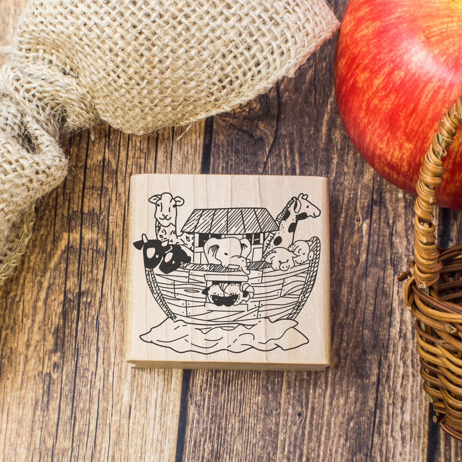 Noahs Ark wooden stamp with cute animals on a rustic wood background, burlap fabric, and apple basket