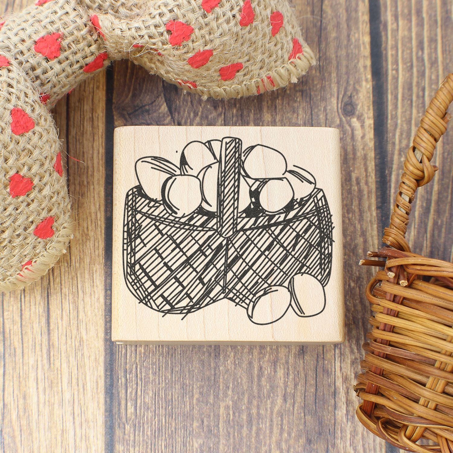 Wooden rubber stamp with basket of eggs illustration on rustic wood background with wicker and burlap decor.