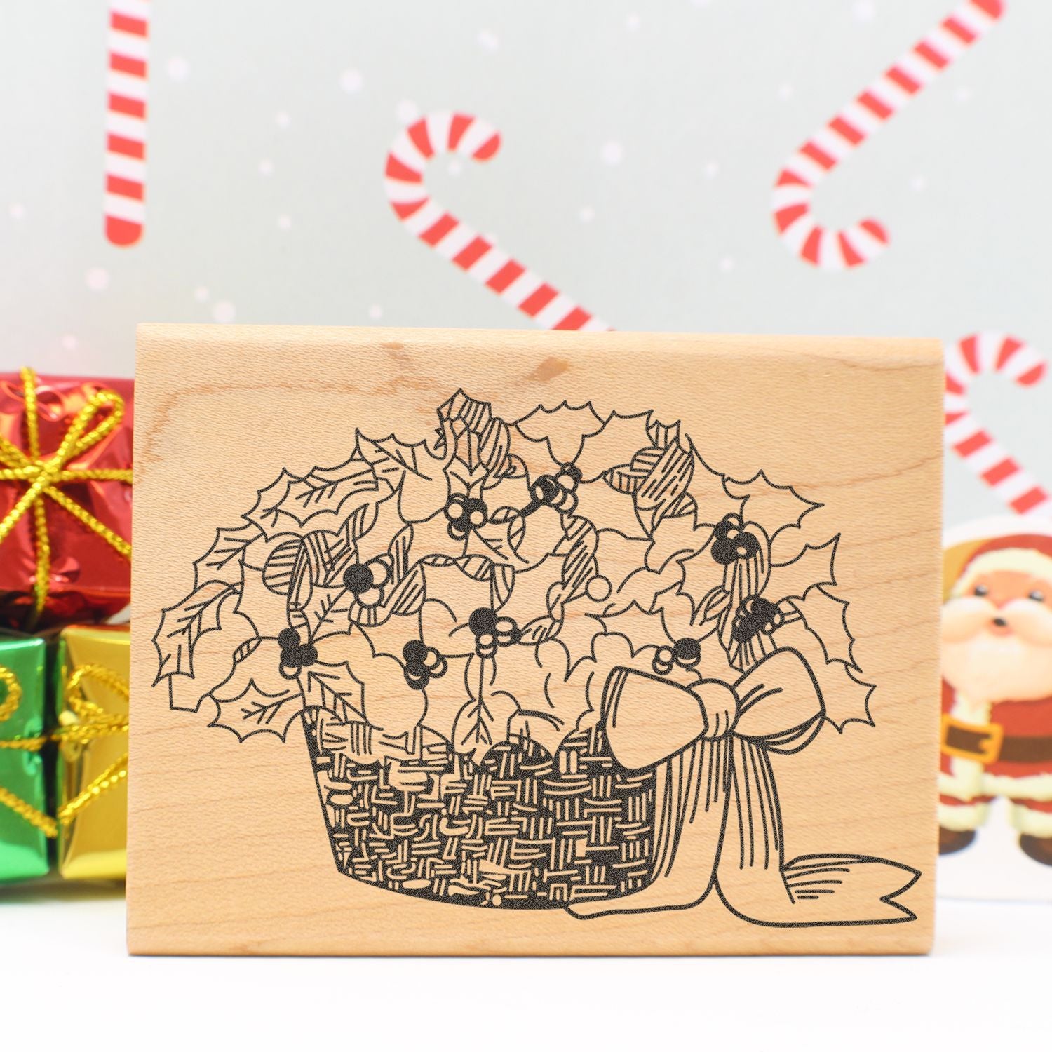 Wooden Christmas stamp with holly basket design, festive holiday craft decor, candy cane background and wrapped gifts.