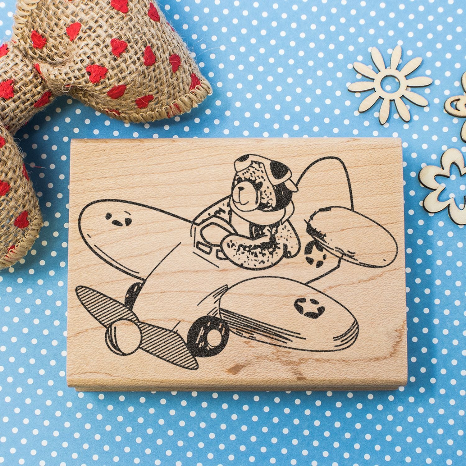 Wooden rubber stamp with vintage dog pilot airplane design on blue polka dot background.