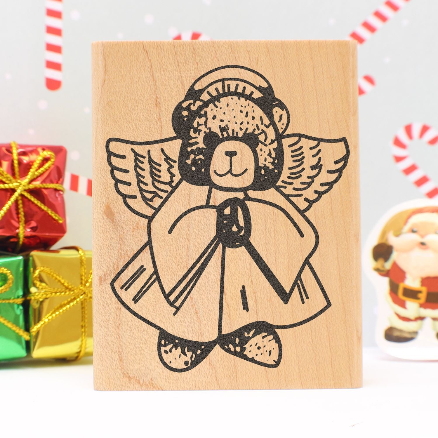 Wooden stamp with angel teddy bear design, festive Christmas gift wrapping and holiday decorations background.