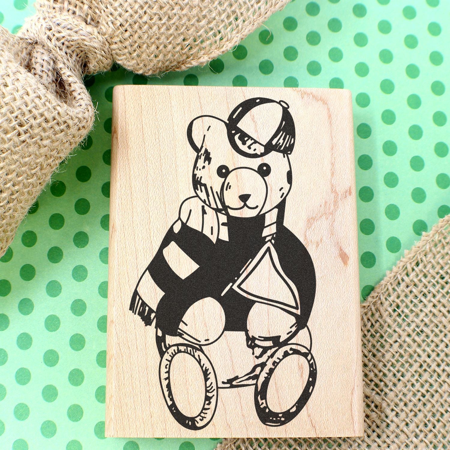 Wooden teddy bear stamp on green polka dot background with burlap fabric accents.