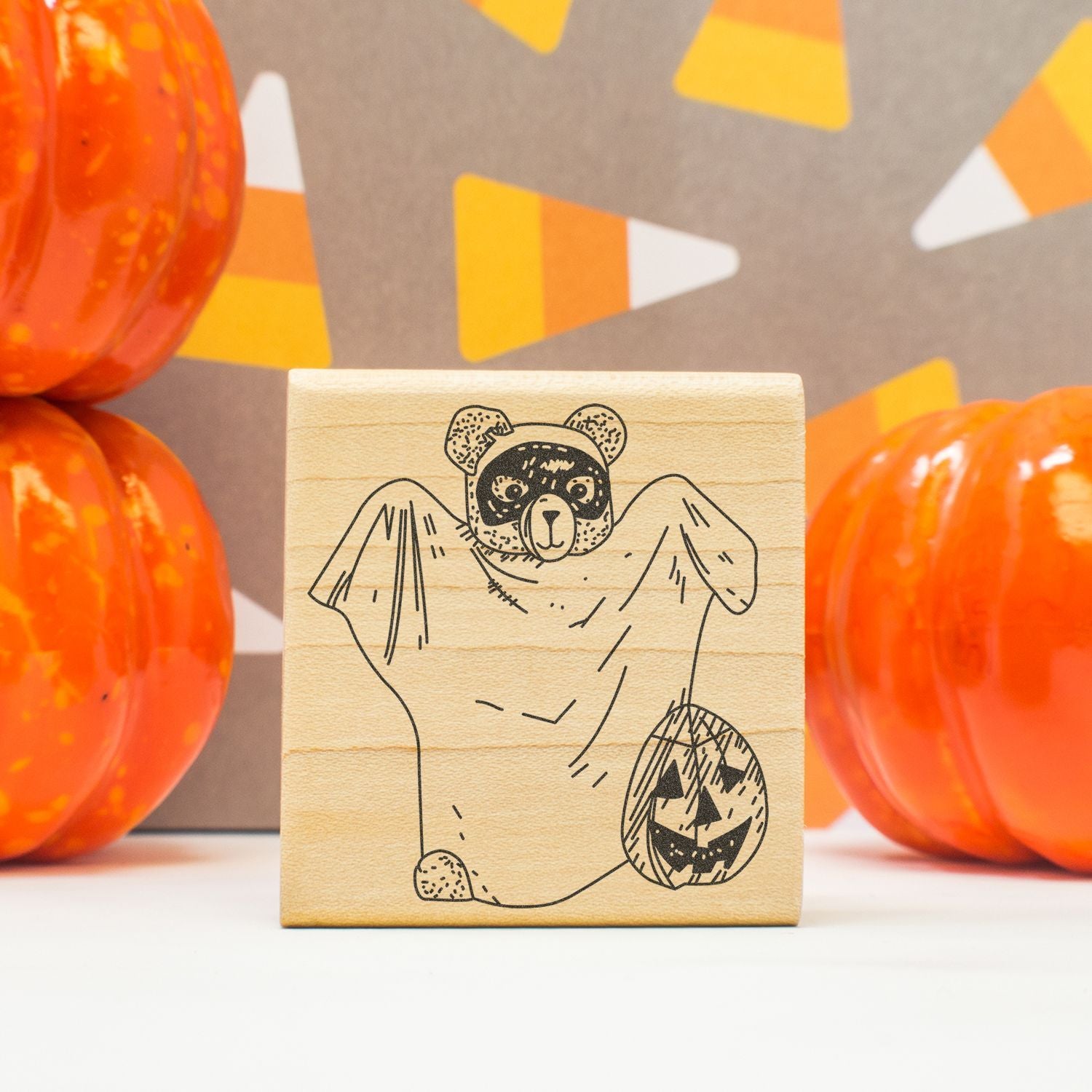 Halloween bear ghost stamp with pumpkin, surrounded by orange decorative pumpkins.