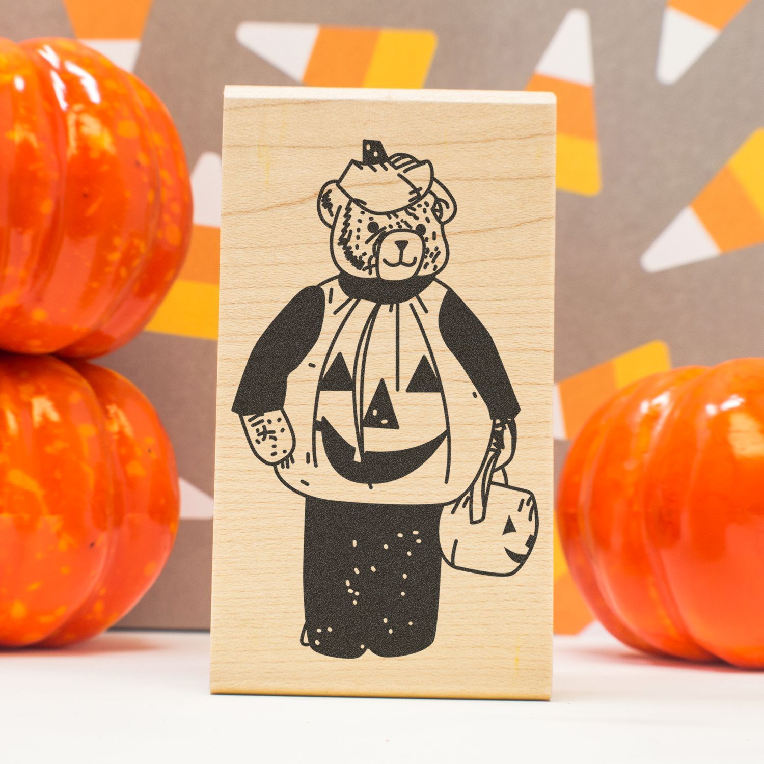 Halloween bear pumpkin stamp on a wooden block with orange decorative pumpkins in the background.