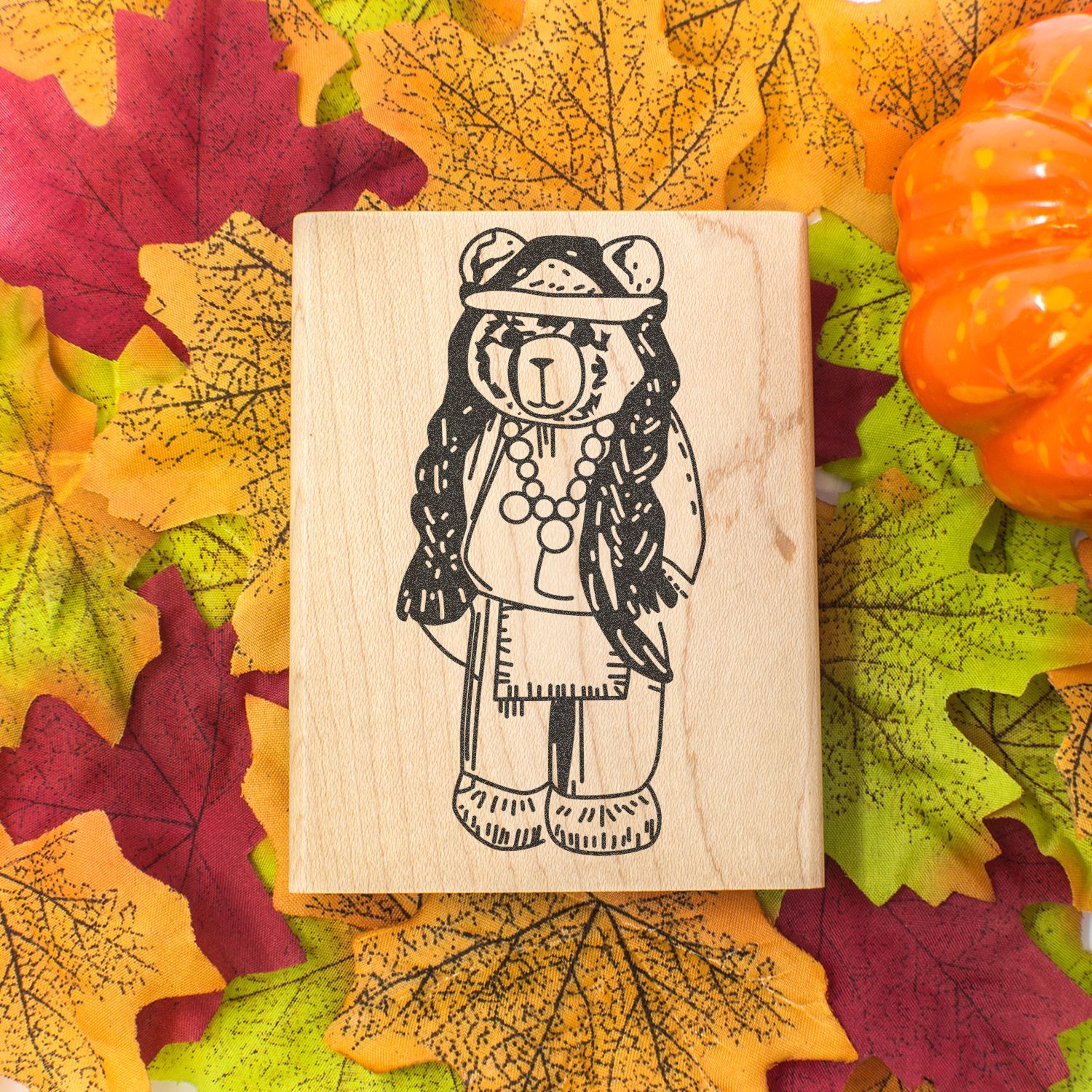 Wooden bear stamp on autumn leaves with Halloween pumpkin decor.