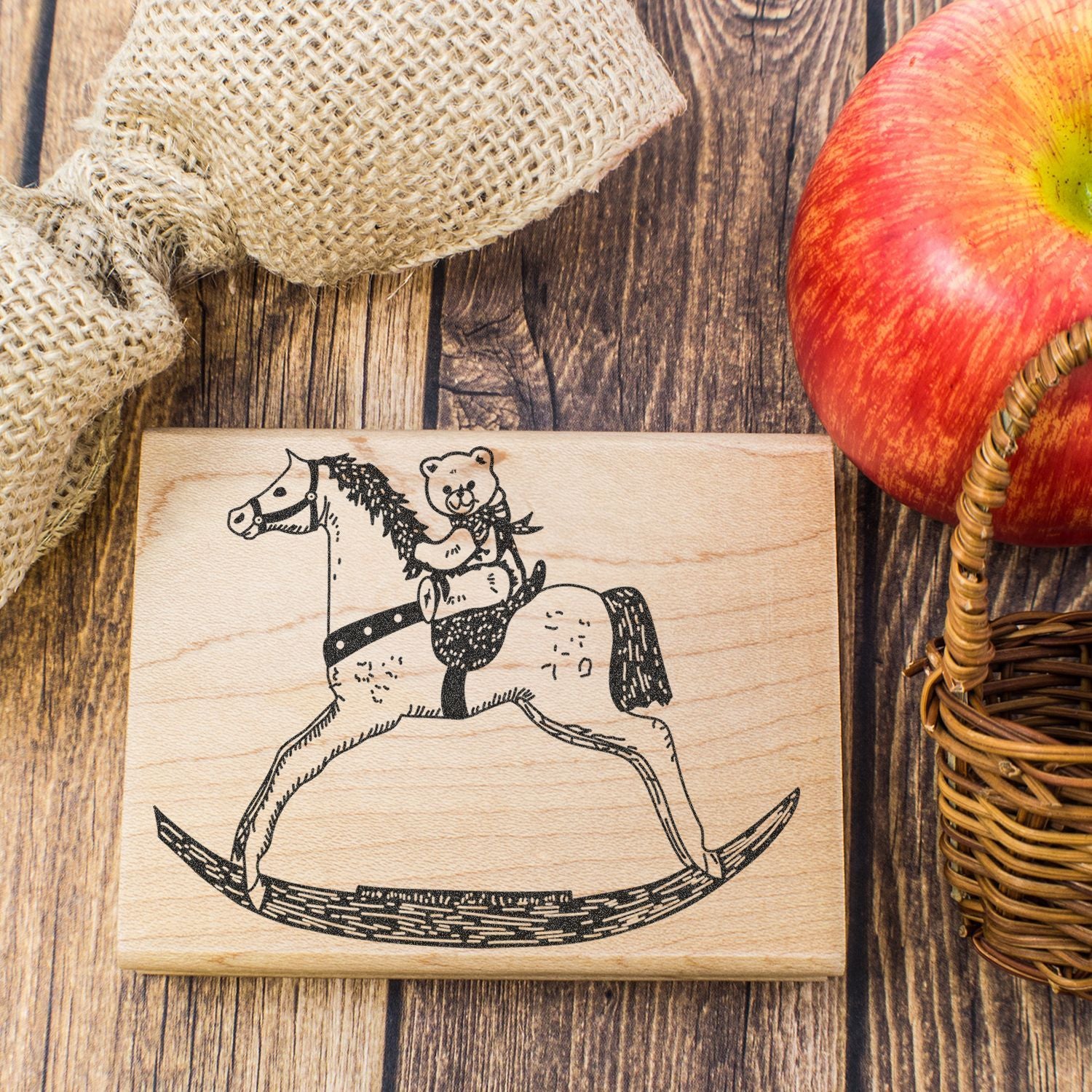Rustic wooden stamp with rocking horse and teddy bear design on a farmhouse table with burlap and an apple