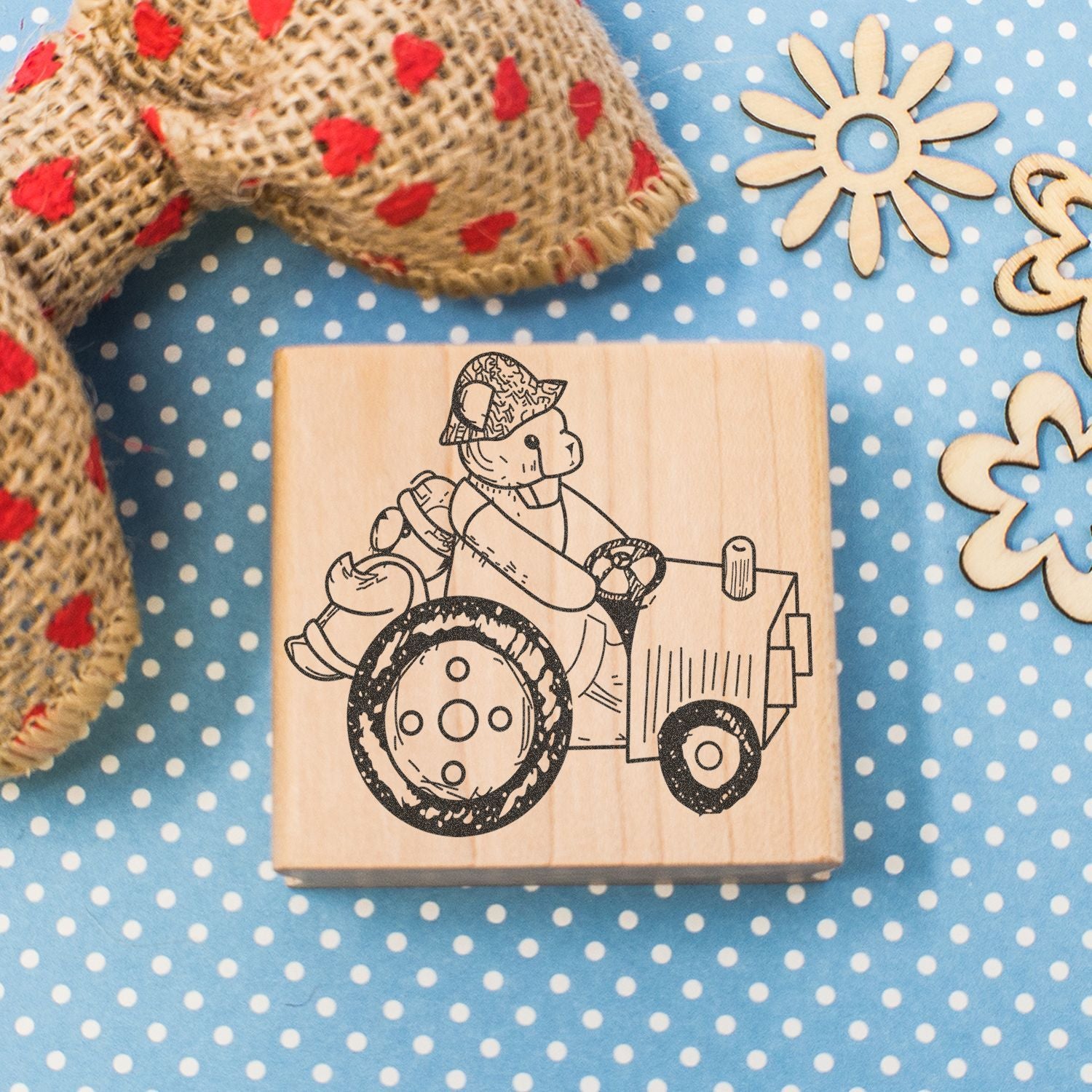 Wooden rubber stamp with bear driving a tractor on blue polka dot background with burlap ribbon and wooden flower decorations
