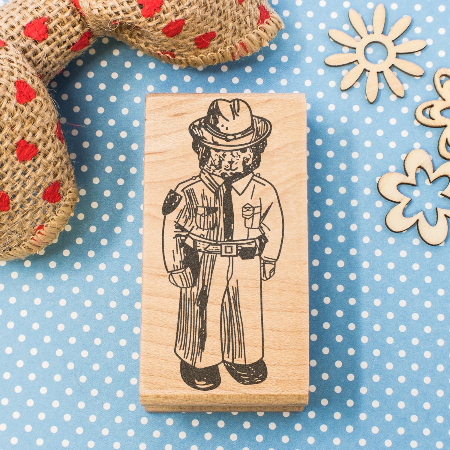 Wooden rubber stamp with vintage cowboy character design on blue polka dot fabric, surrounded by rustic rope and wooden floral cutouts.