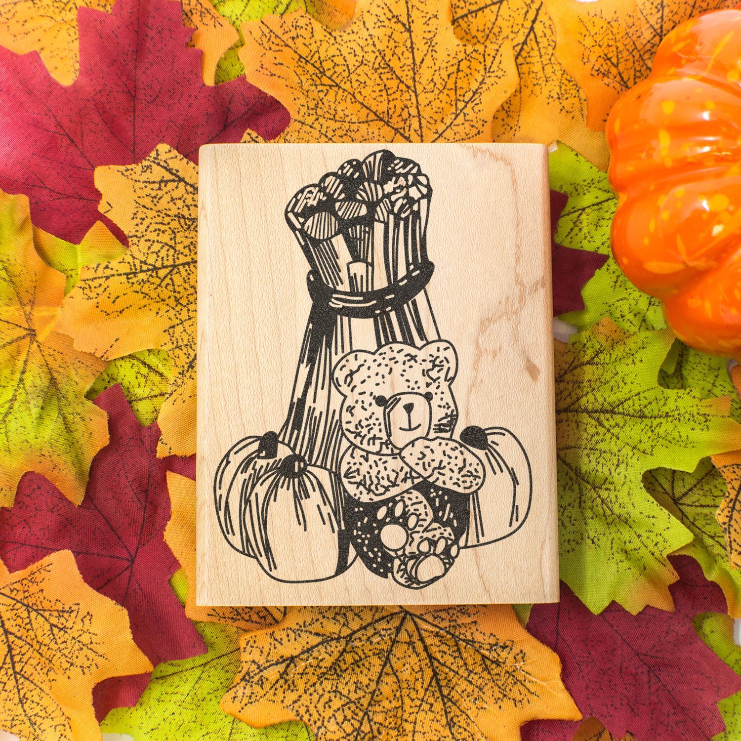 Autumn wooden stamp with teddy bear and pumpkins on fall leaves background.