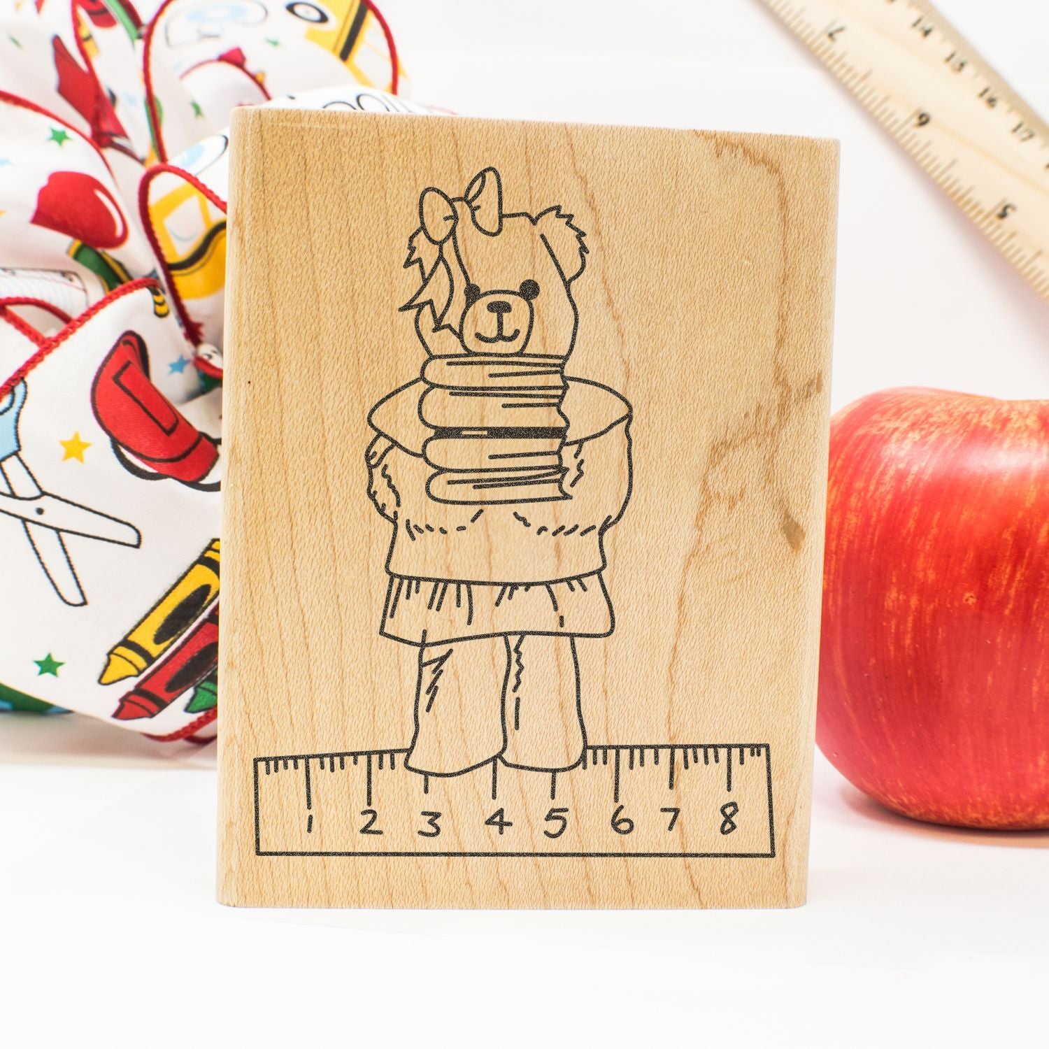 Wooden educational stamp with cute bear on a ruler, school supplies, apple, and measuring tape background