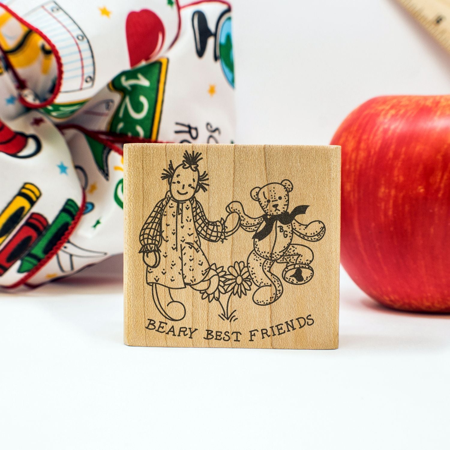 Wooden Beary Best Friends stamp with girl and teddy bear illustration, styled with an apple and colorful fabric background.