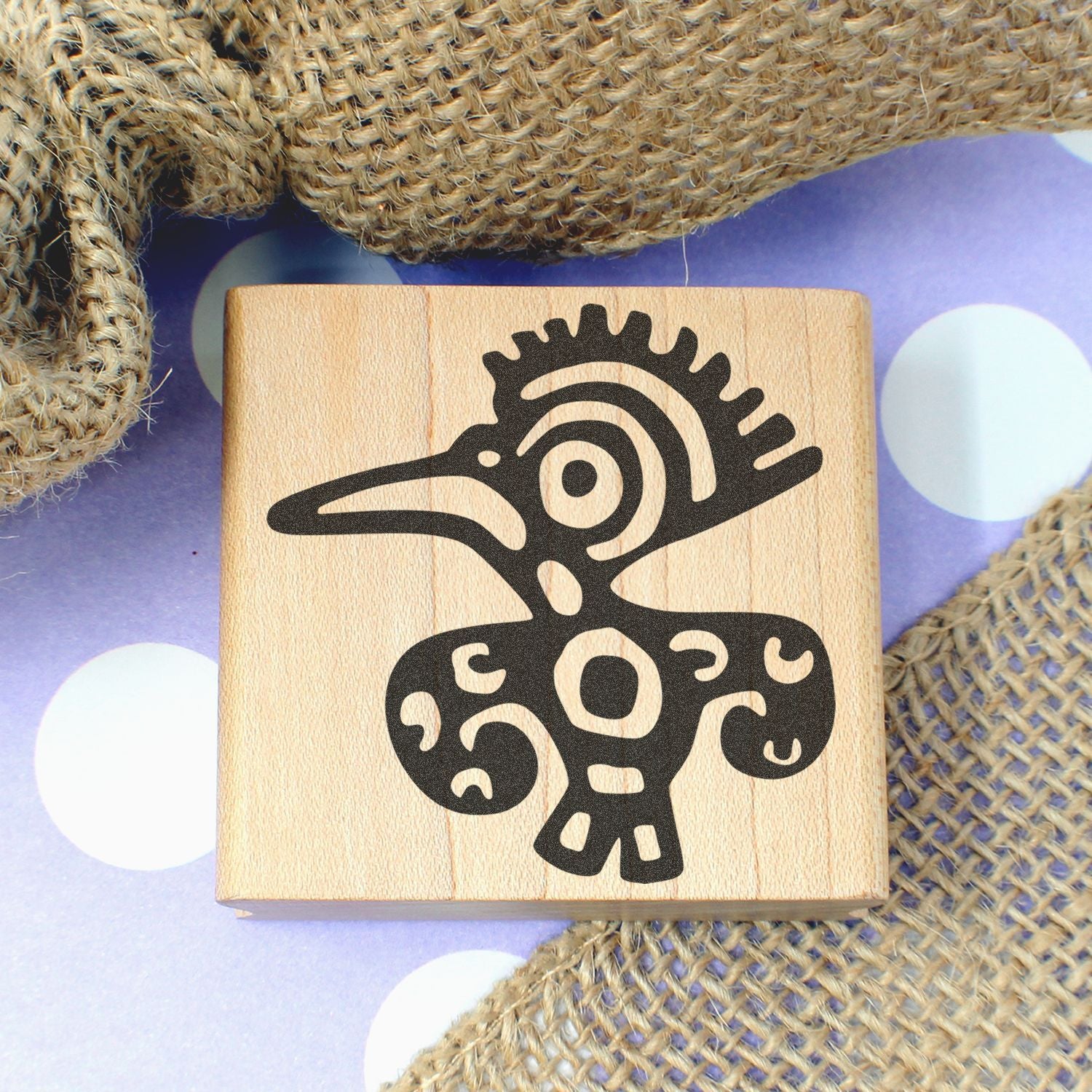 Wooden rubber stamp with tribal bird design on purple polka dot background and burlap fabric.