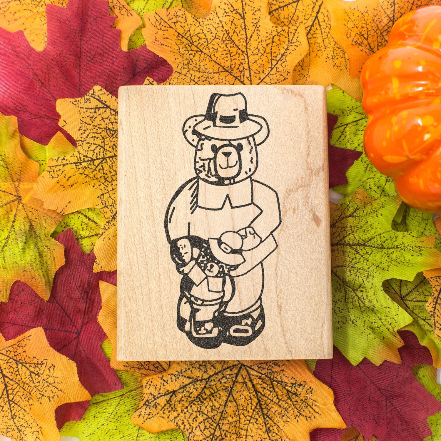 Wooden stamp with cute bear in pilgrim hat on autumn leaves background with pumpkin, Thanksgiving decor design