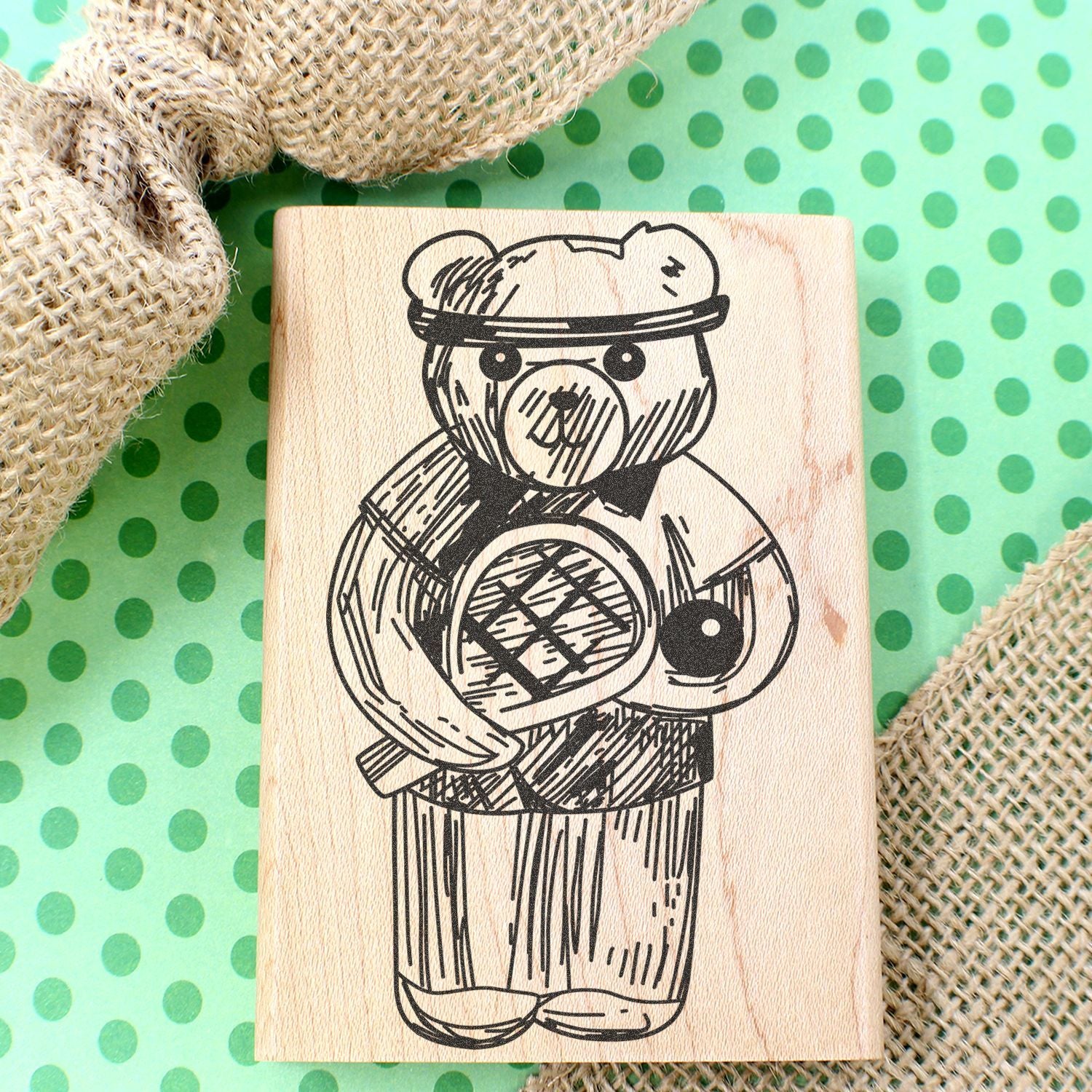 Wooden teddy bear stamp on green polka dot background with burlap decor.