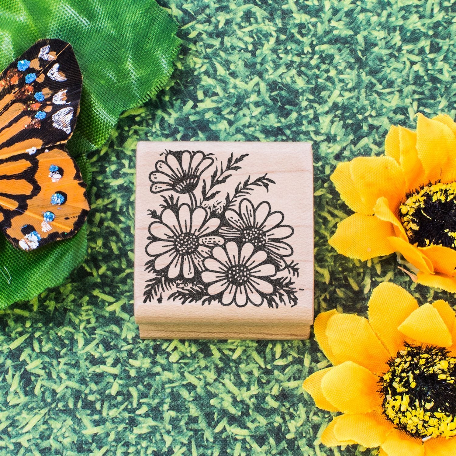 Floral rubber stamp with daisy design, butterfly wing, and yellow sunflowers on a green background