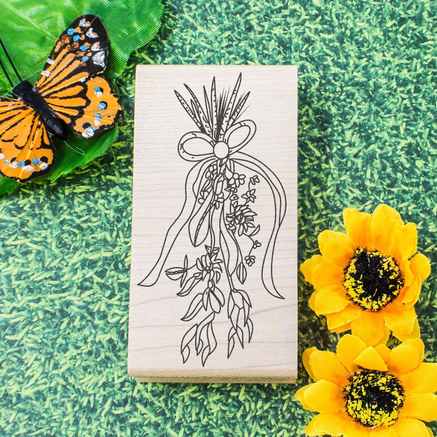 Wooden flower and butterfly stamp with floral wreath design on green background, surrounded by decorative butterfly and yellow flowers
