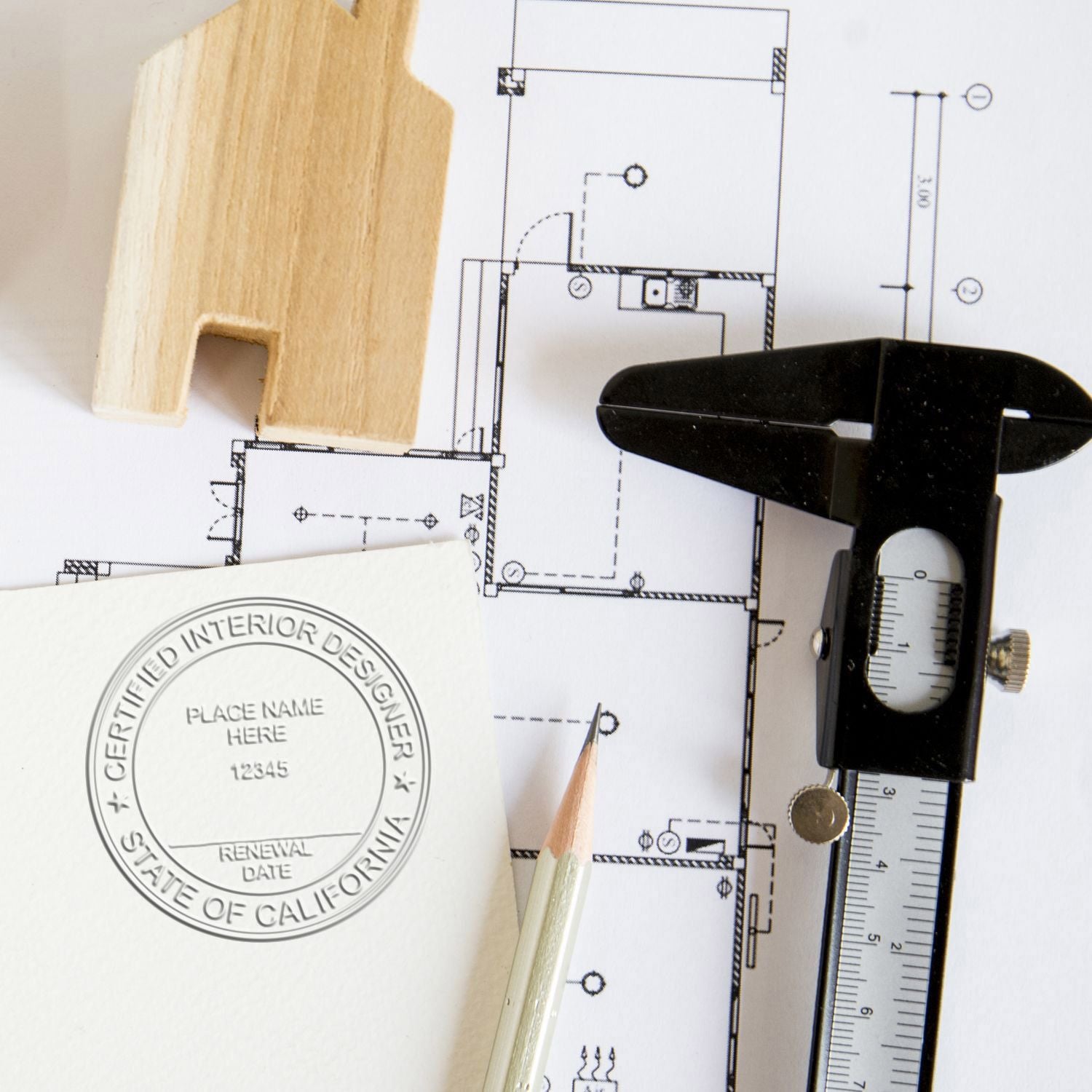 Architectural floor plan with wood sample, caliper, pencil, and certified interior designer stamp for interior design and renovation planning.