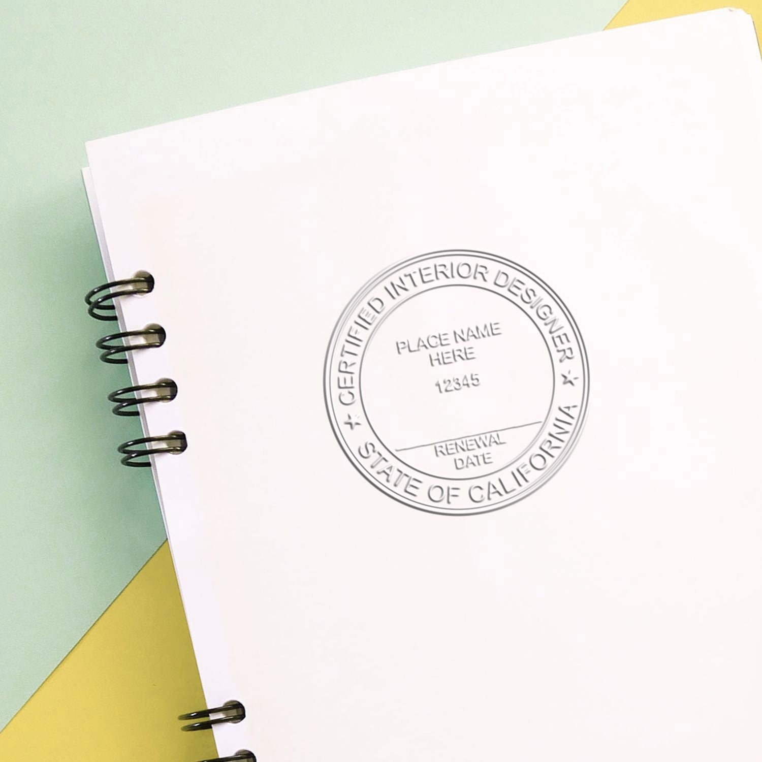 Blank spiral-bound notebook with embossed Certified Interior Designer State of California seal on pastel background.