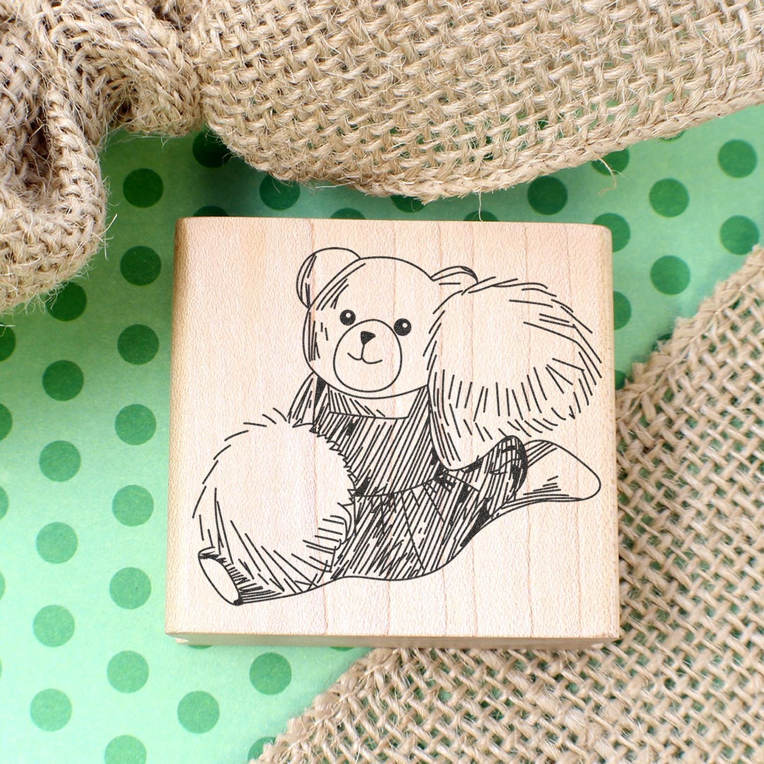 Wooden rubber stamp with cute teddy bear illustration on a green polka dot background and burlap fabric.