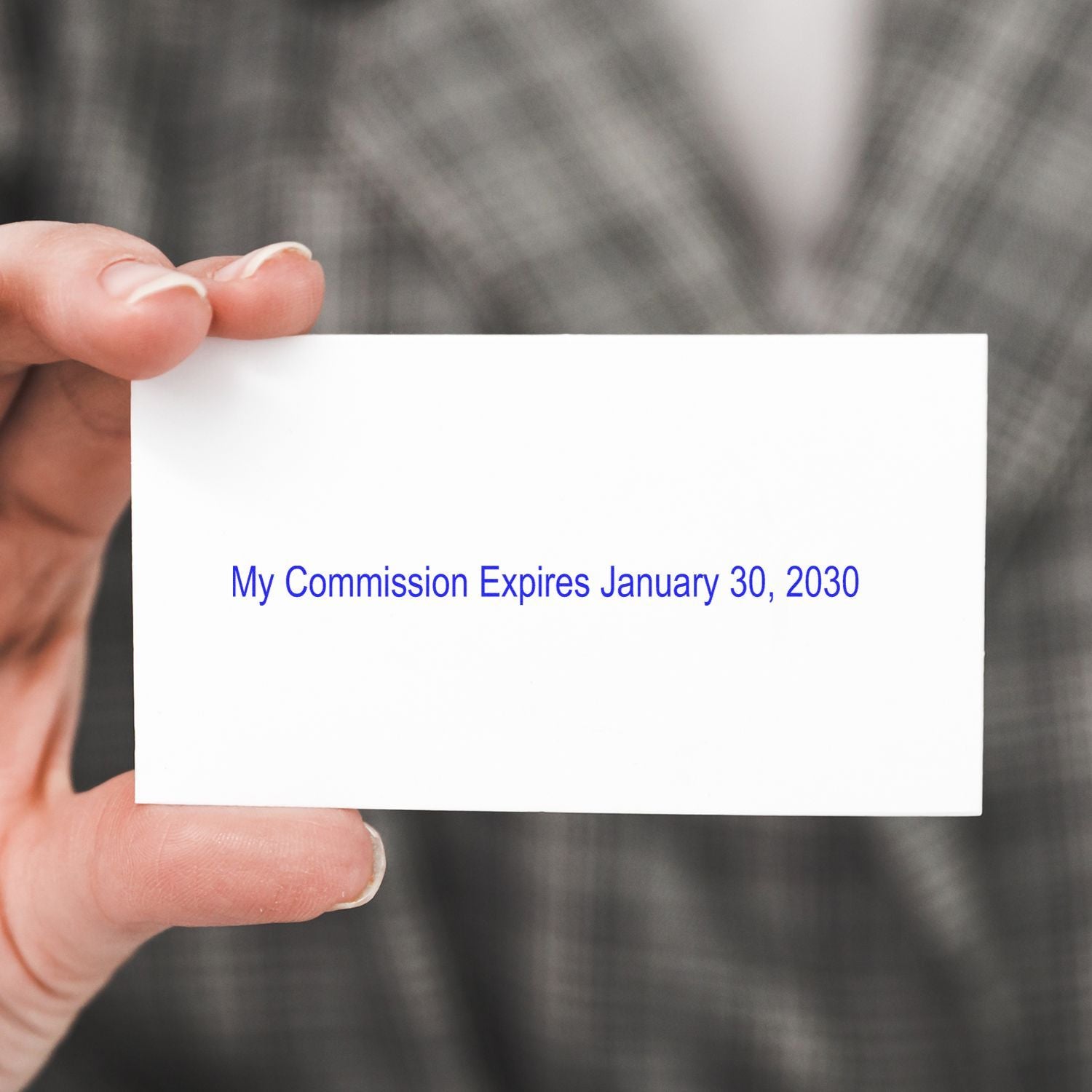 Hand holding a white business card reading My Commission Expires January 30, 2030 against a blurred background.