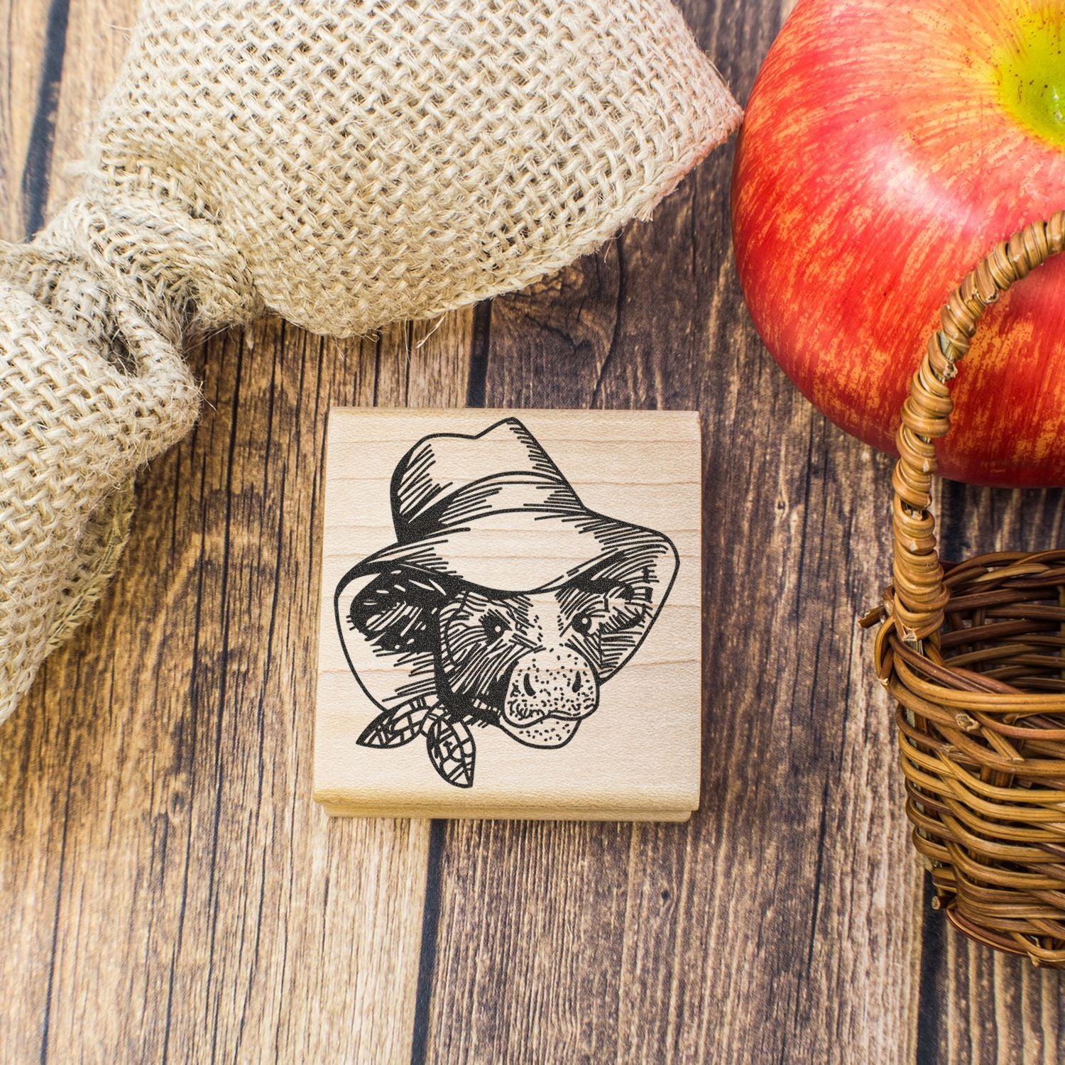 Rustic wooden rubber stamp with bear illustration, apple, burlap sack, and wicker basket on a farmhouse wood background