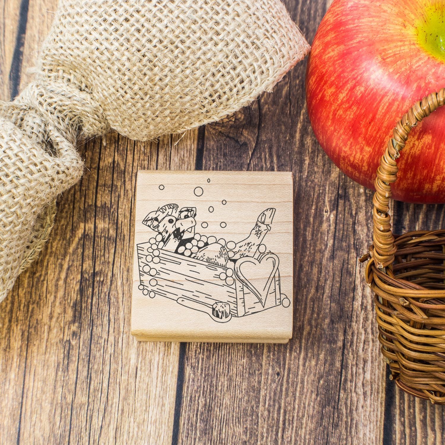 Rustic apple-themed rubber stamp on wooden background with burlap, wicker basket, and red apple.