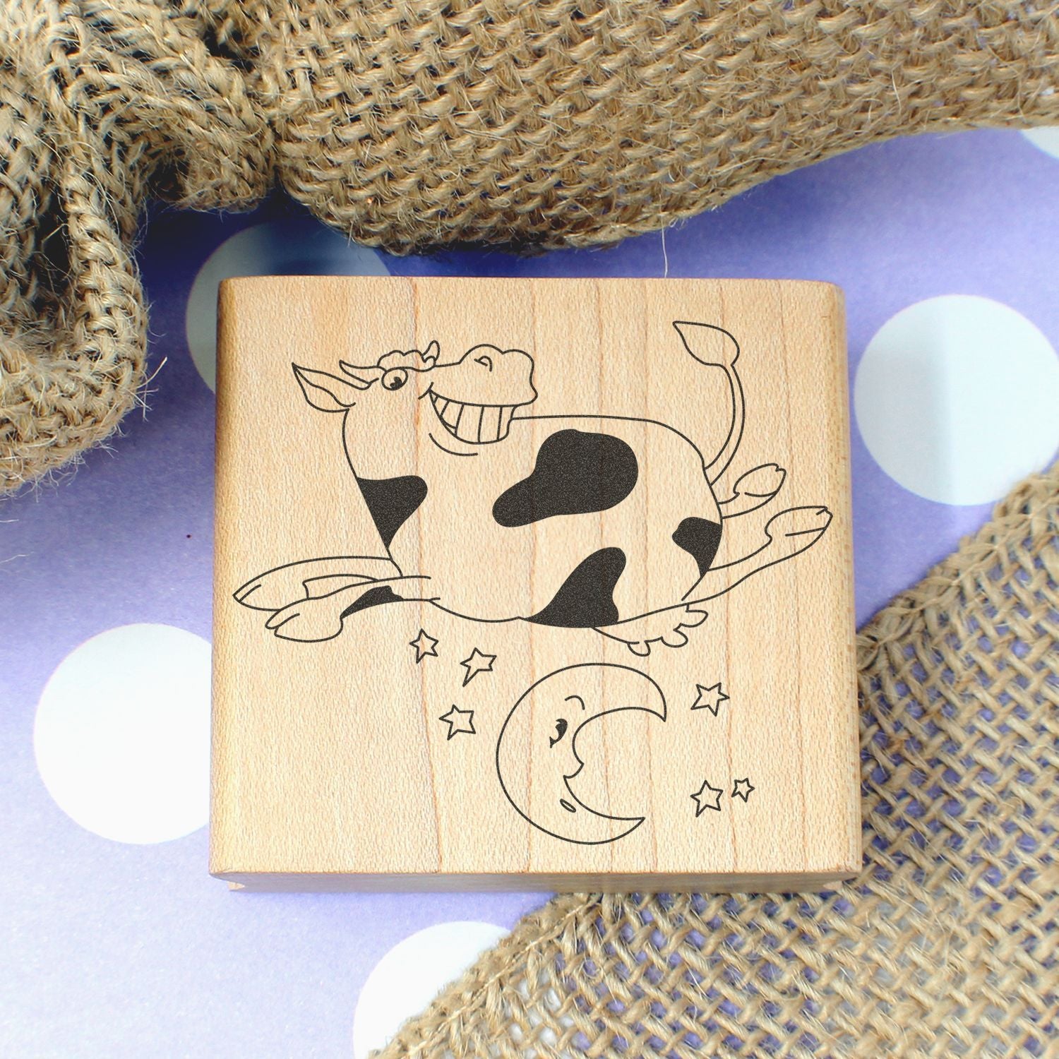 Wooden cow and moon stamp with cute farm animal design on a purple polka dot background with burlap fabric.