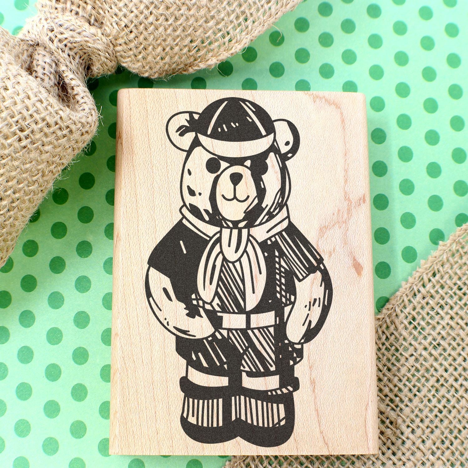 Wooden block stamp with a cute pirate bear illustration on a green polka dot background with burlap fabric.