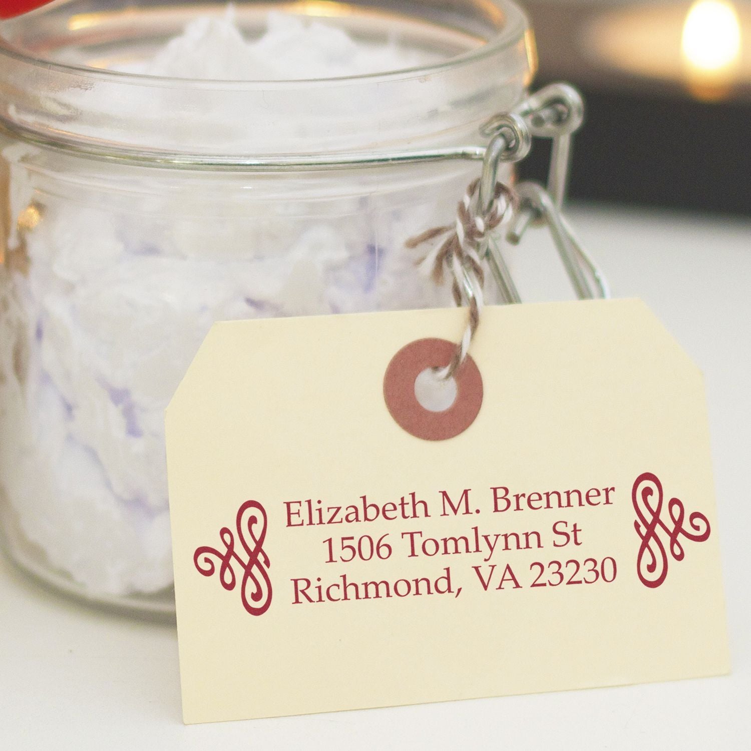 Personalized address rubber stamp on gift tag tied to glass jar, featuring custom name and return address imprint.