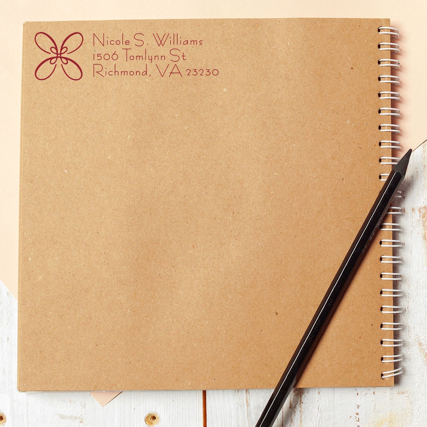 Custom return address rubber stamp impression on kraft notebook cover with floral monogram, name, and address.